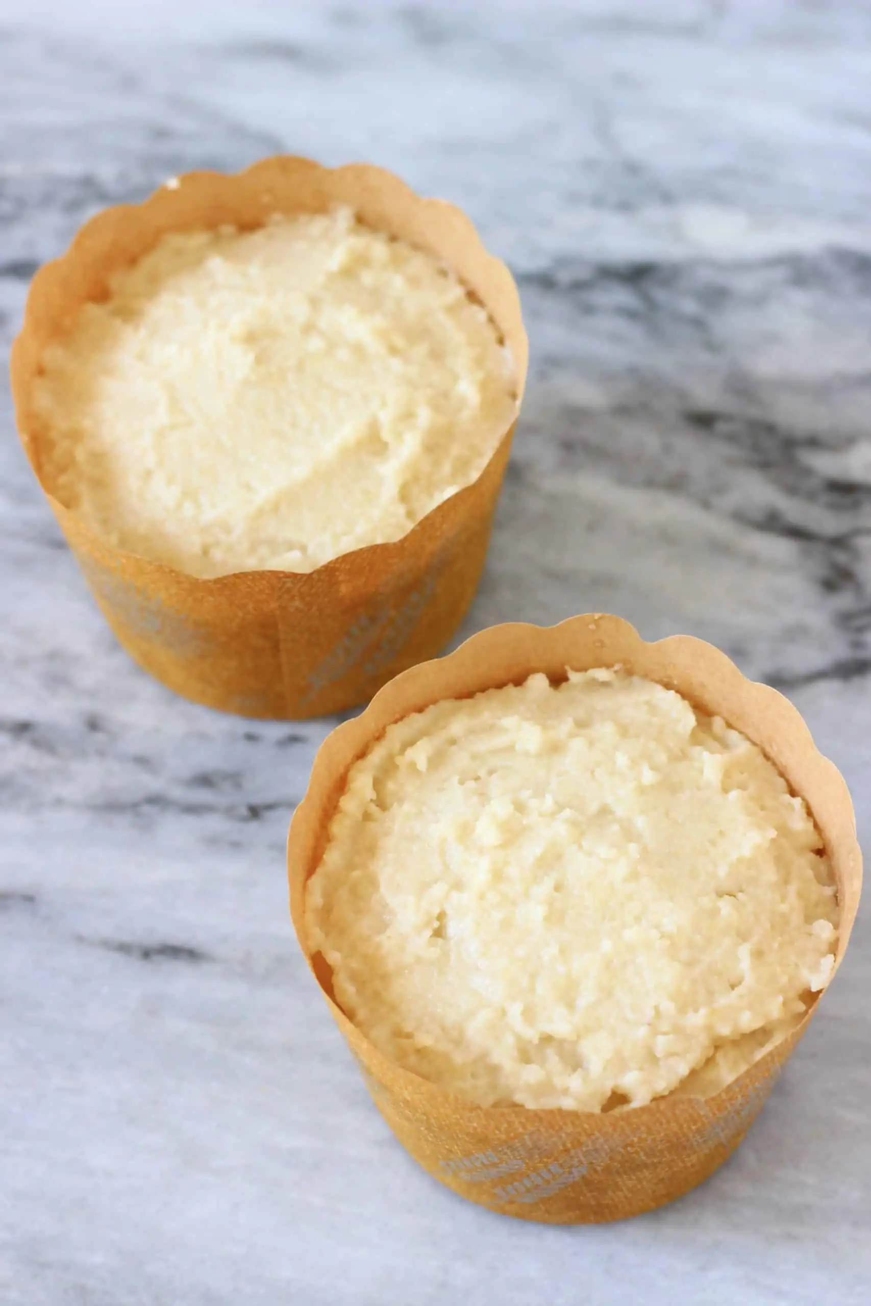 Two brown muffin bases filled with gluten-free vegan lemon muffin batter