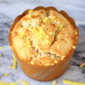 A gluten-free vegan lemon muffin in a brown muffin case topped with lemon zest