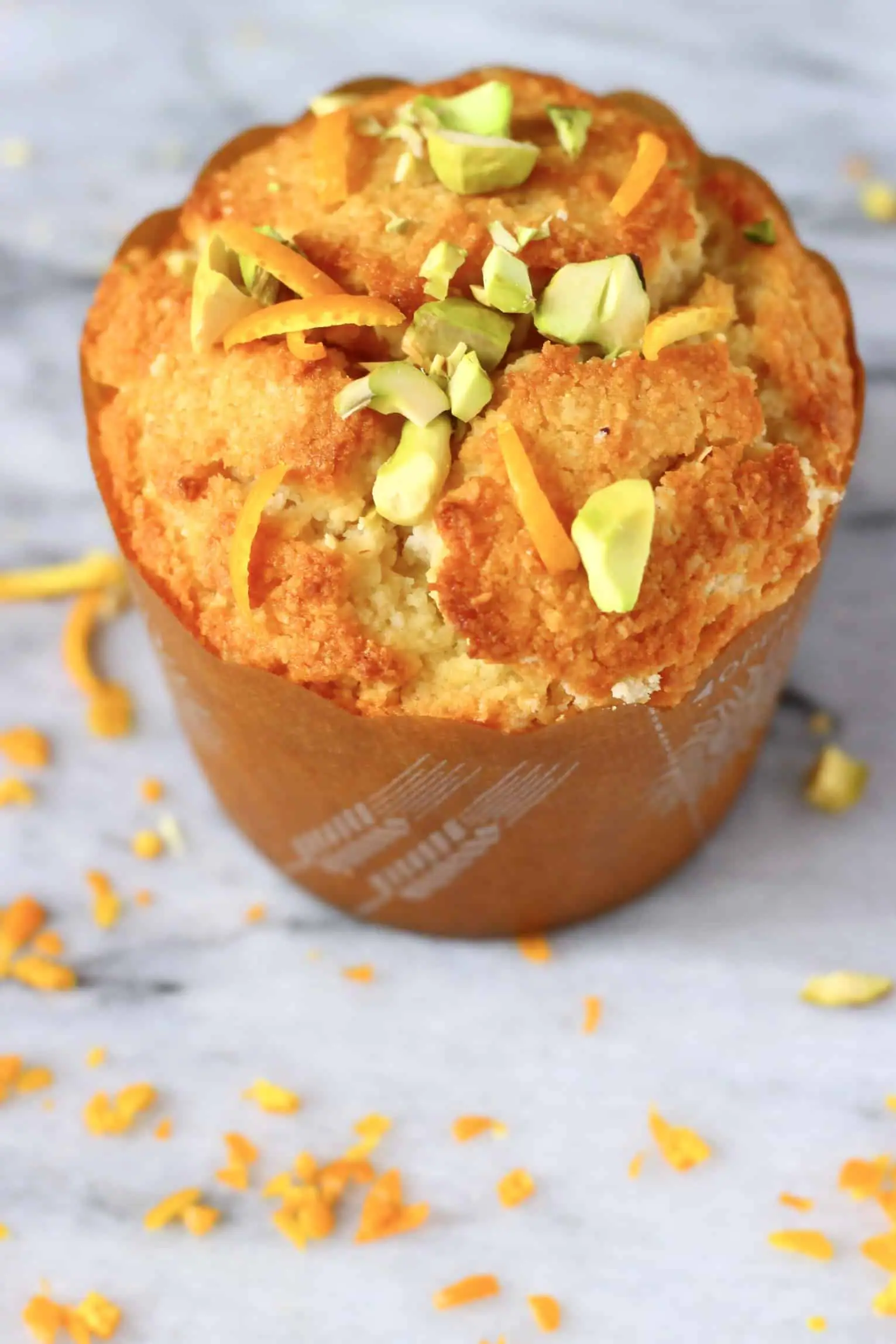 A gluten-free vegan orange muffin in a brown muffin case topped with chopped pistachios
