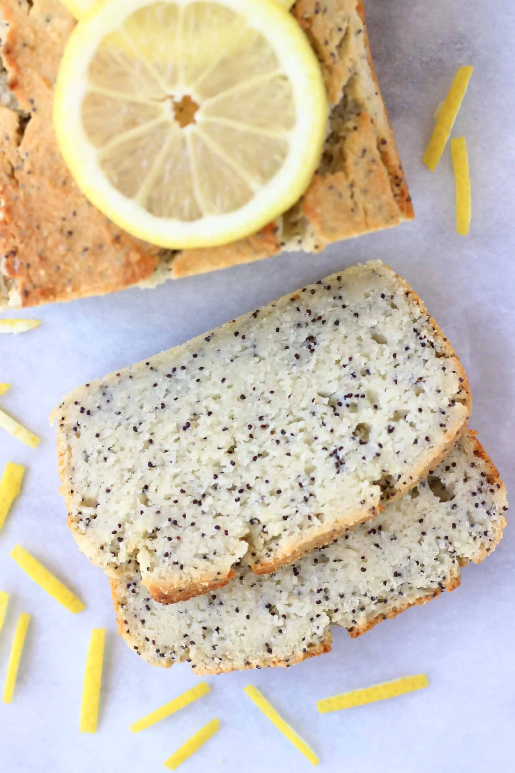 A loaf of gluten-free vegan lemon poppy seed bread with two slices next to it topped with lemon slices