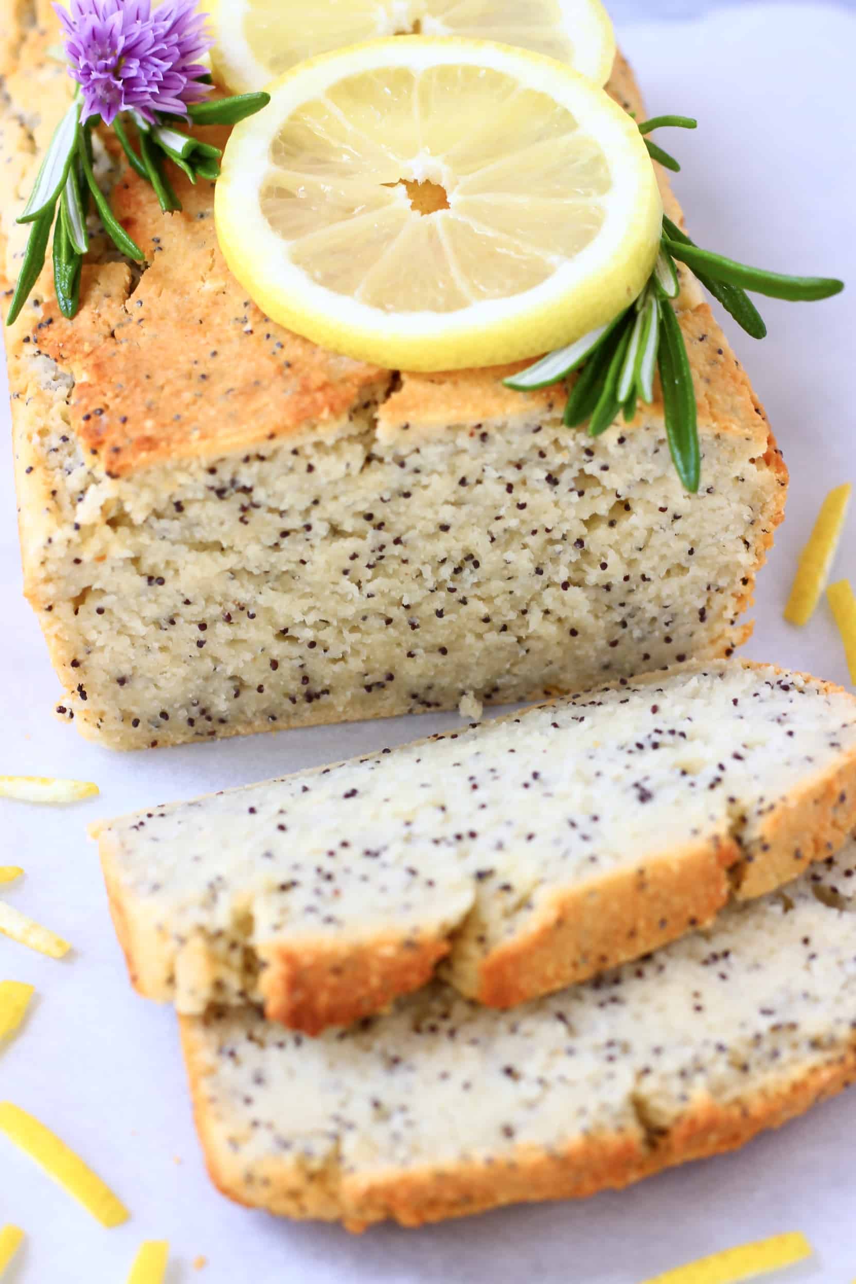 A loaf of gluten-free vegan lemon poppy seed bread with two slices next to it topped with lemon slices