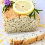 A loaf of gluten-free vegan lemon poppy seed bread with two slices next to it topped with lemon slices
