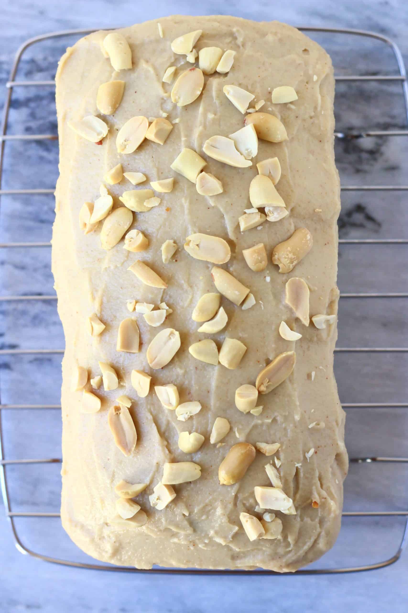 Peanut butter frosting spread over a loaf of banana bread with chopped peanuts on a wire rack