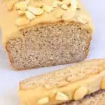 A loaf of gluten-free vegan peanut butter banana bread with peanut butter frosting with two slices next to it