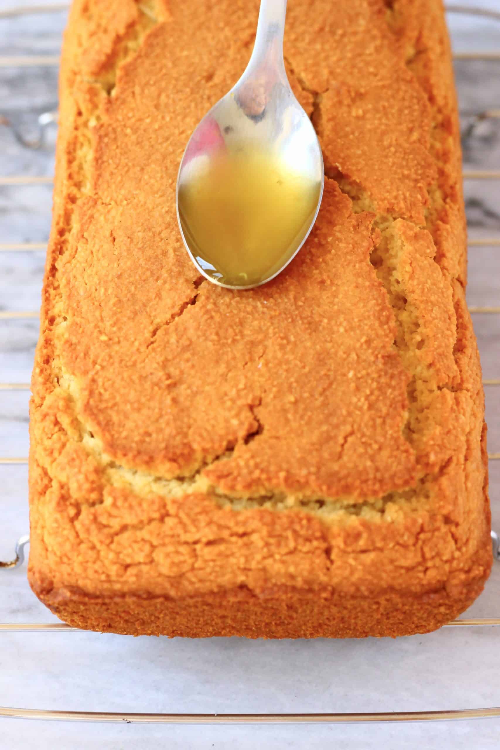 A loaf of gluten-free vegan orange drizzle cake on a wire rack with a spoon pouring syrup on top