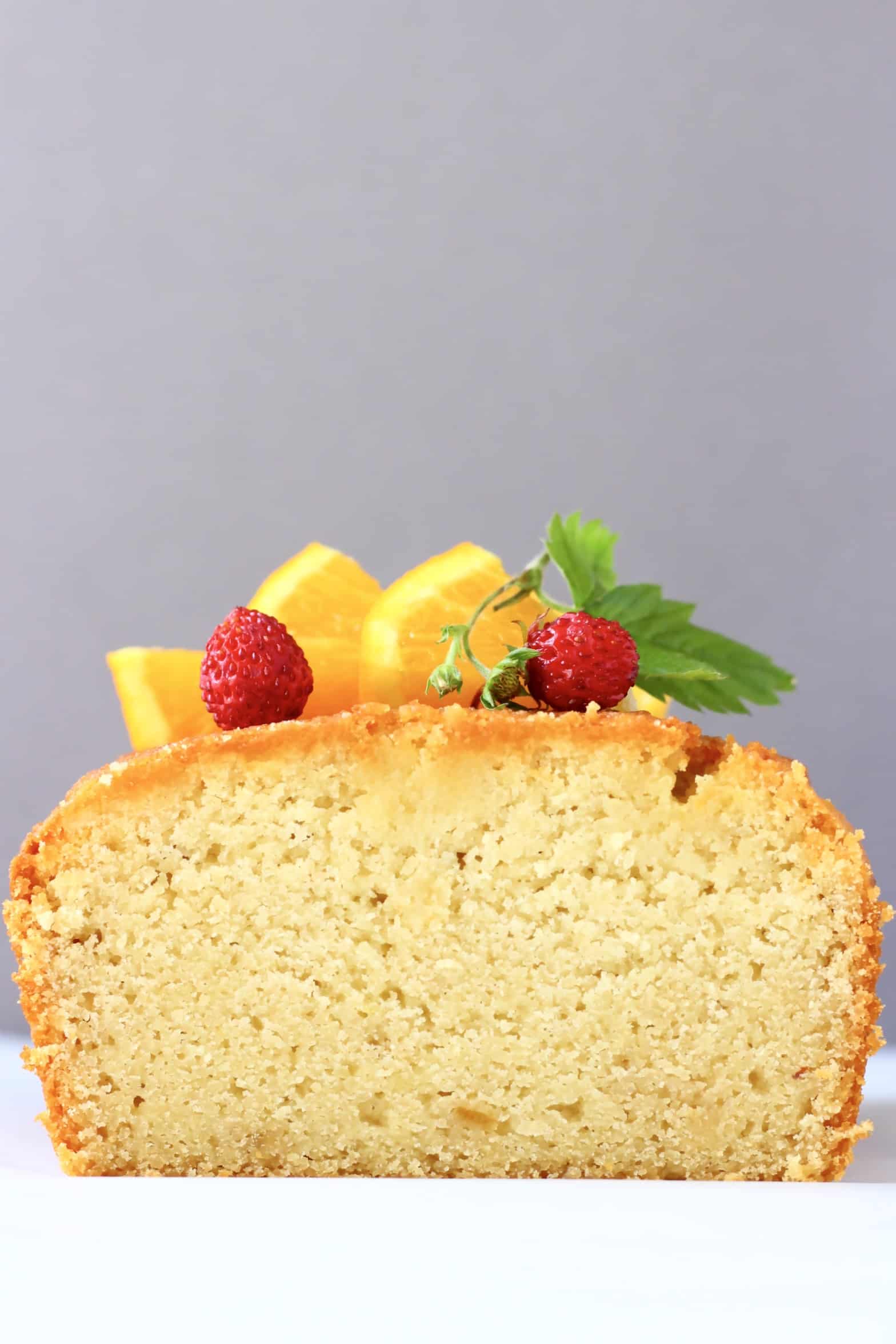 A sliced loaf of gluten-free vegan orange drizzle cake topped with orange slices