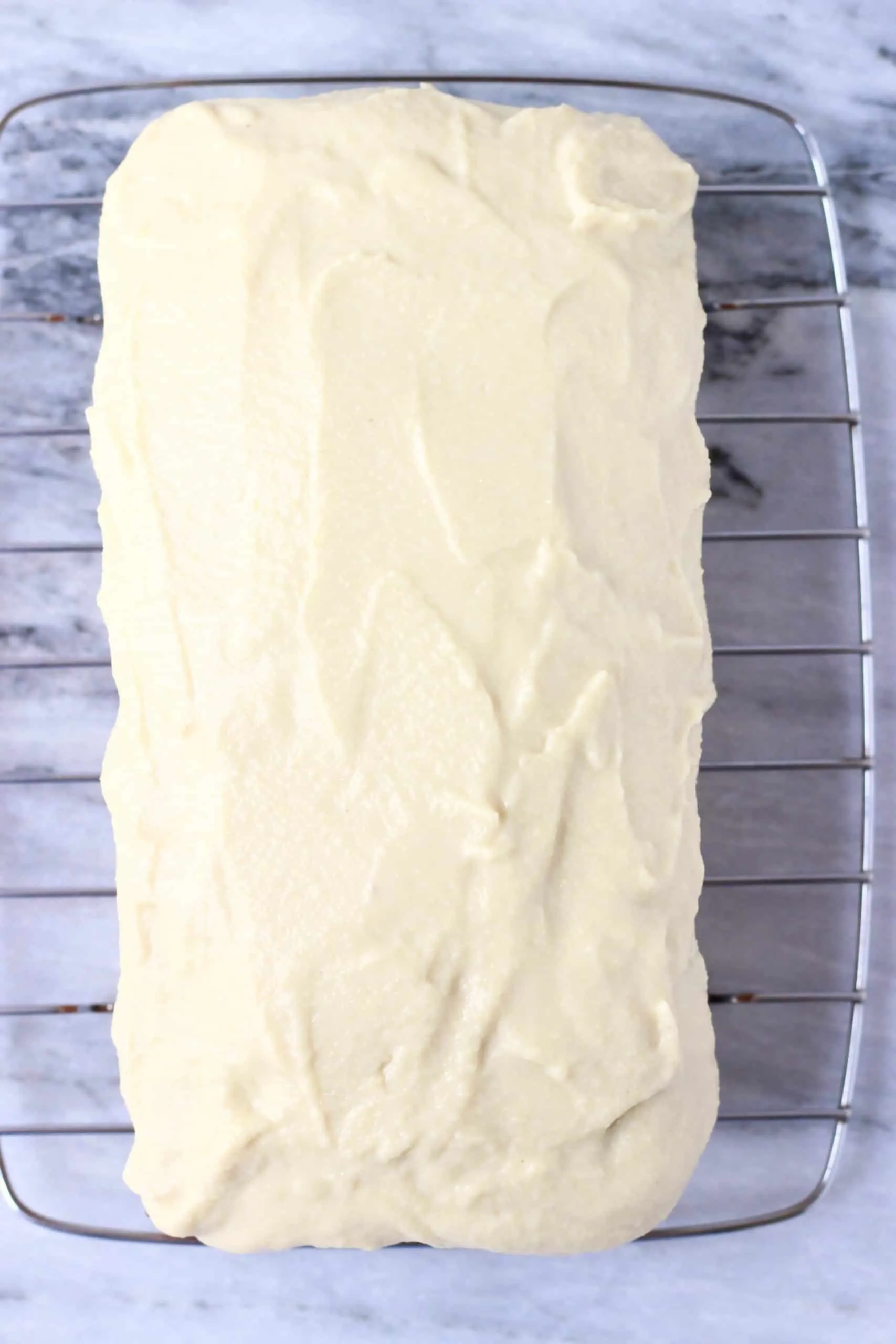 A loaf of gluten-free vegan lemon bread on a wire rack topped with frosting