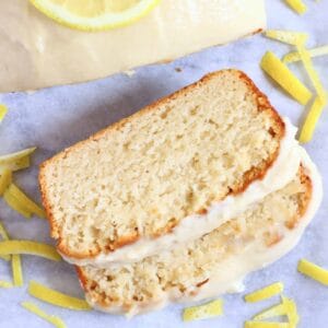 A loaf of gluten-free vegan lemon bread topped with frosting with two slices next to it