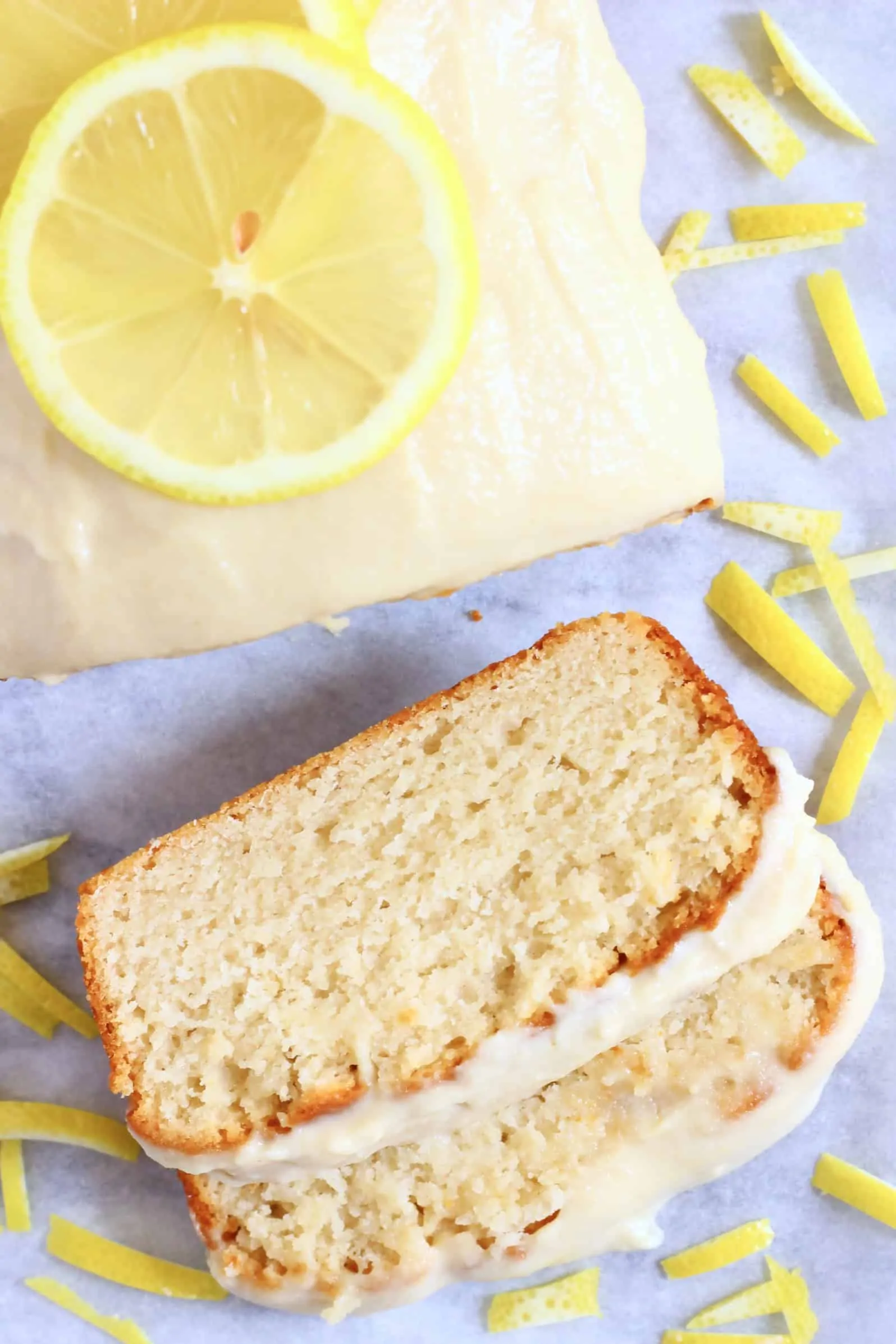 A loaf of gluten-free vegan lemon bread topped with frosting with two slices next to it