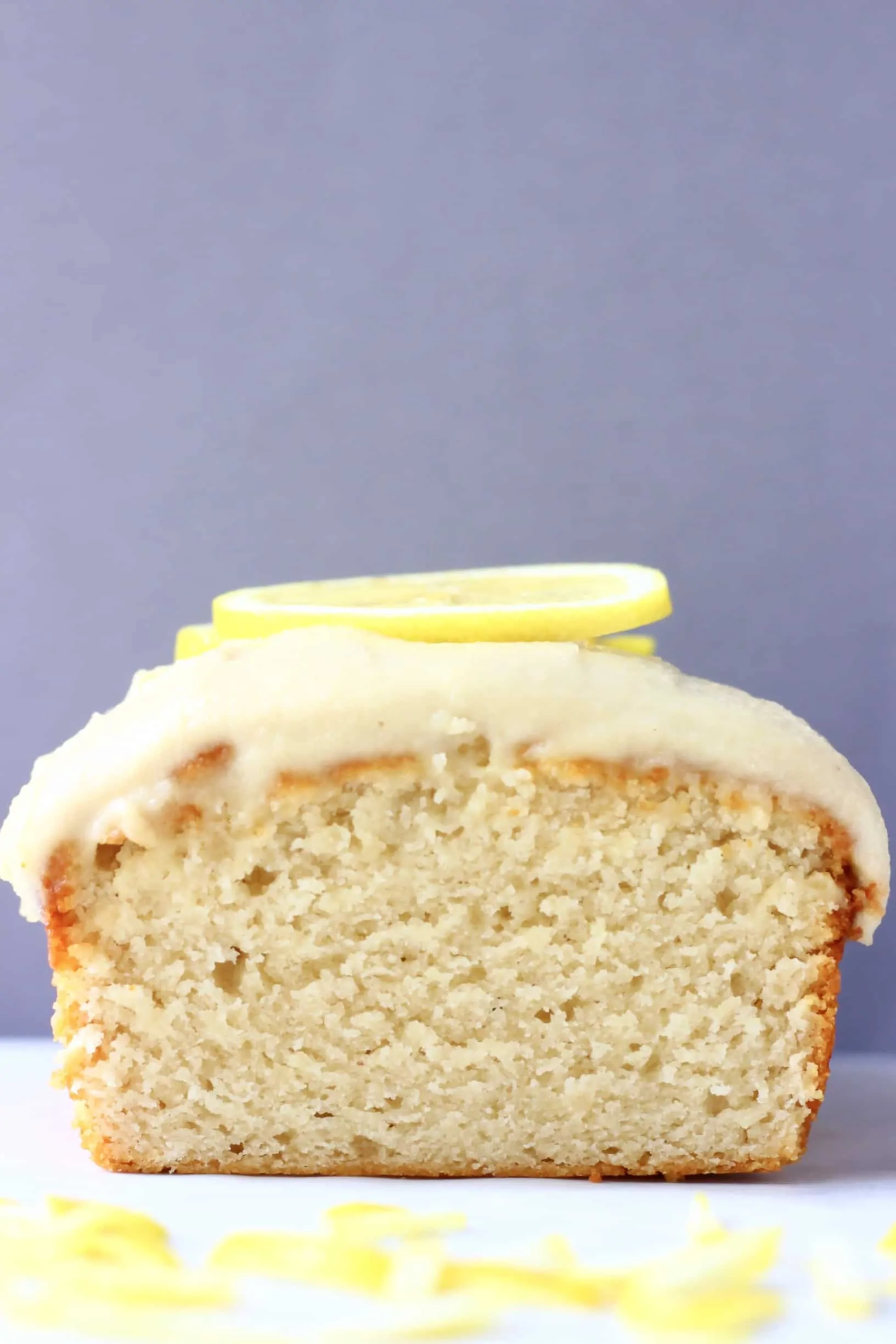 A sliced loaf of gluten-free vegan lemon bread topped with frosting and lemon slices