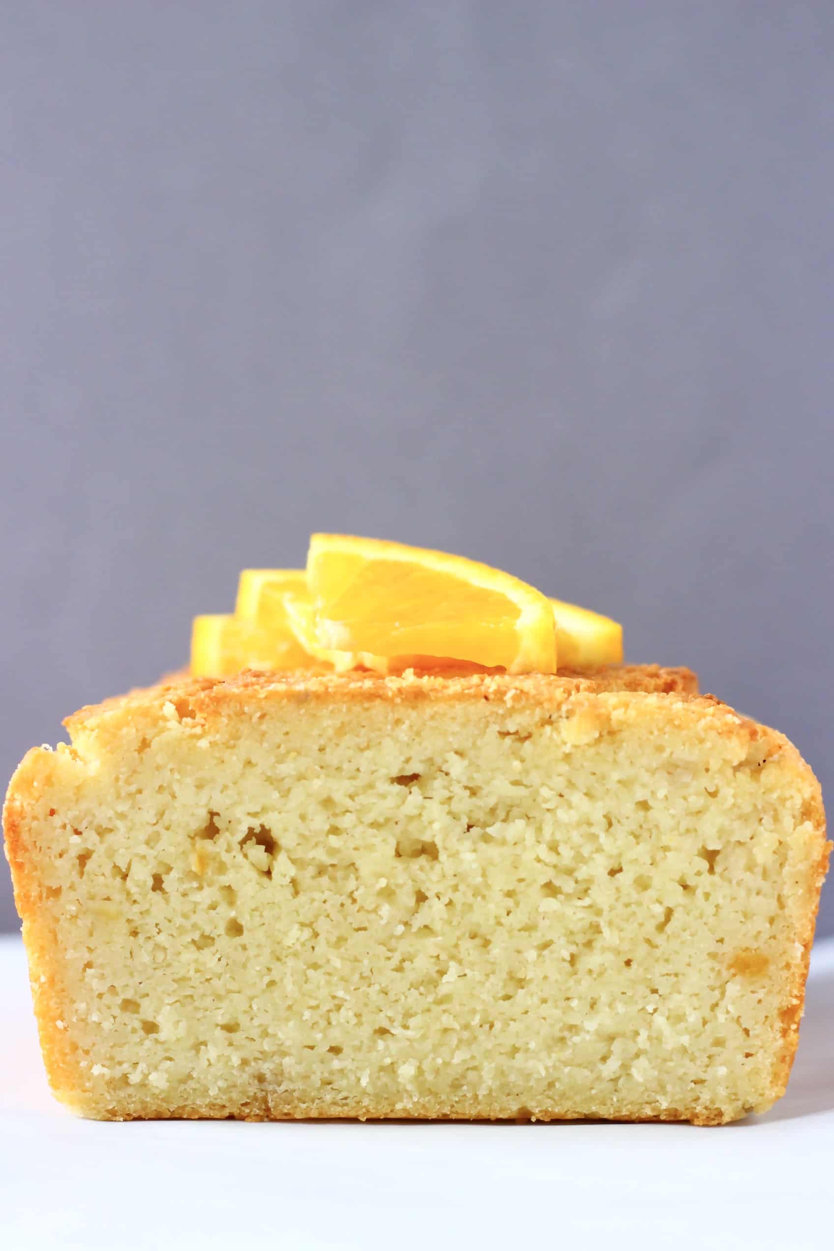 A sliced gluten-free vegan orange pound cake topped with orange wedges