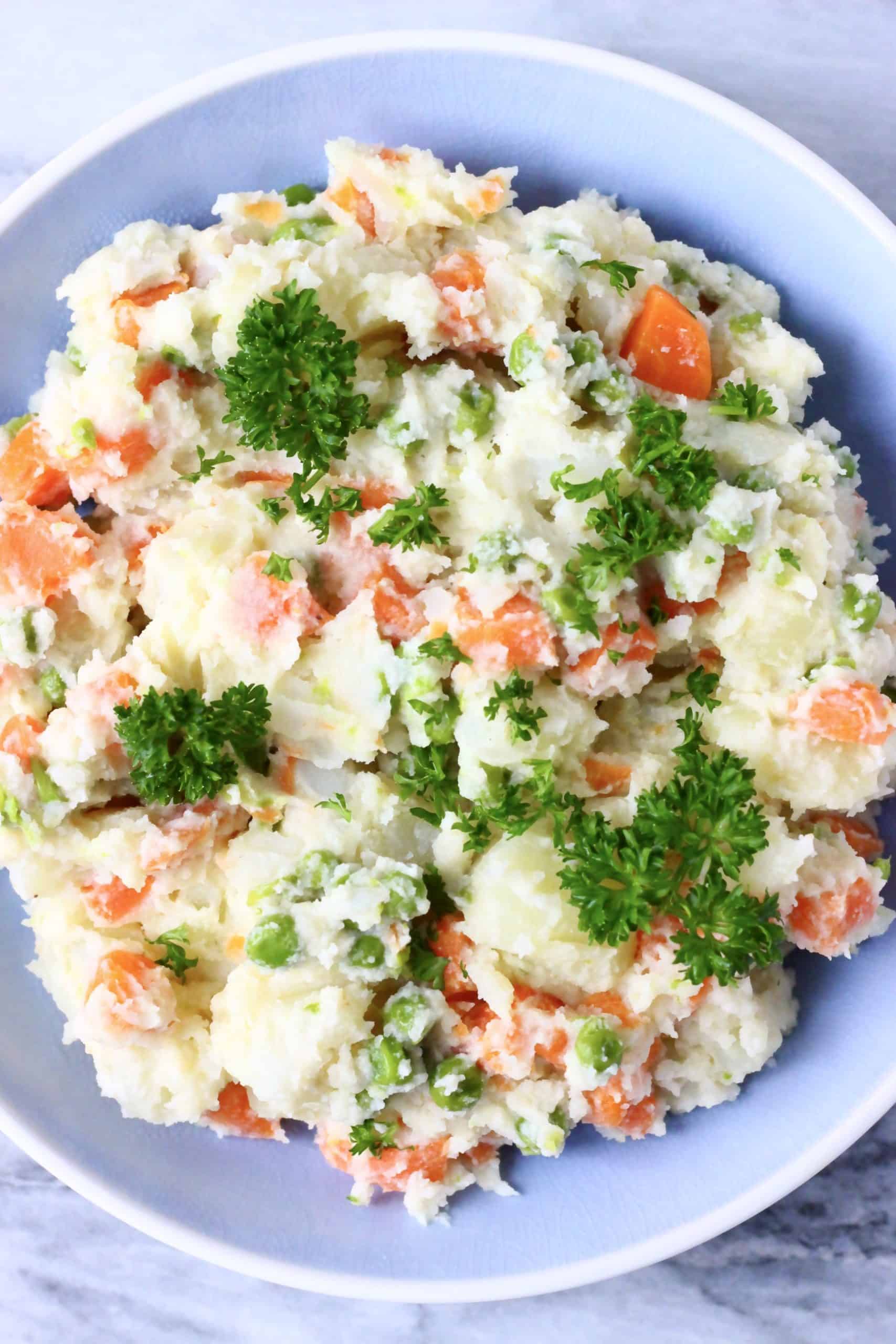 Vegan potato salad with peas and carrots in a blue bowl