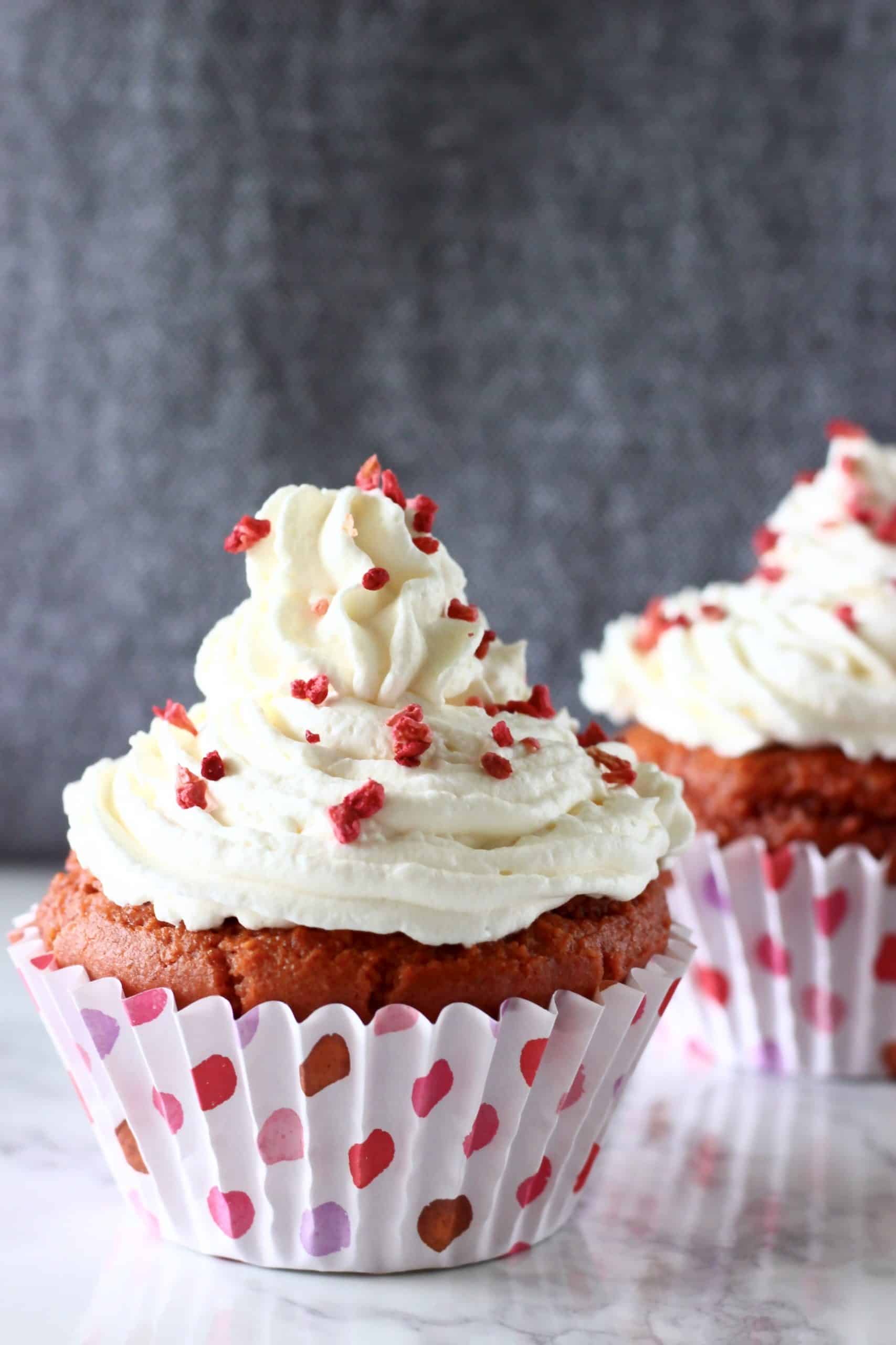 Two gluten-free vegan red velvet cupcakes topped with white frosting