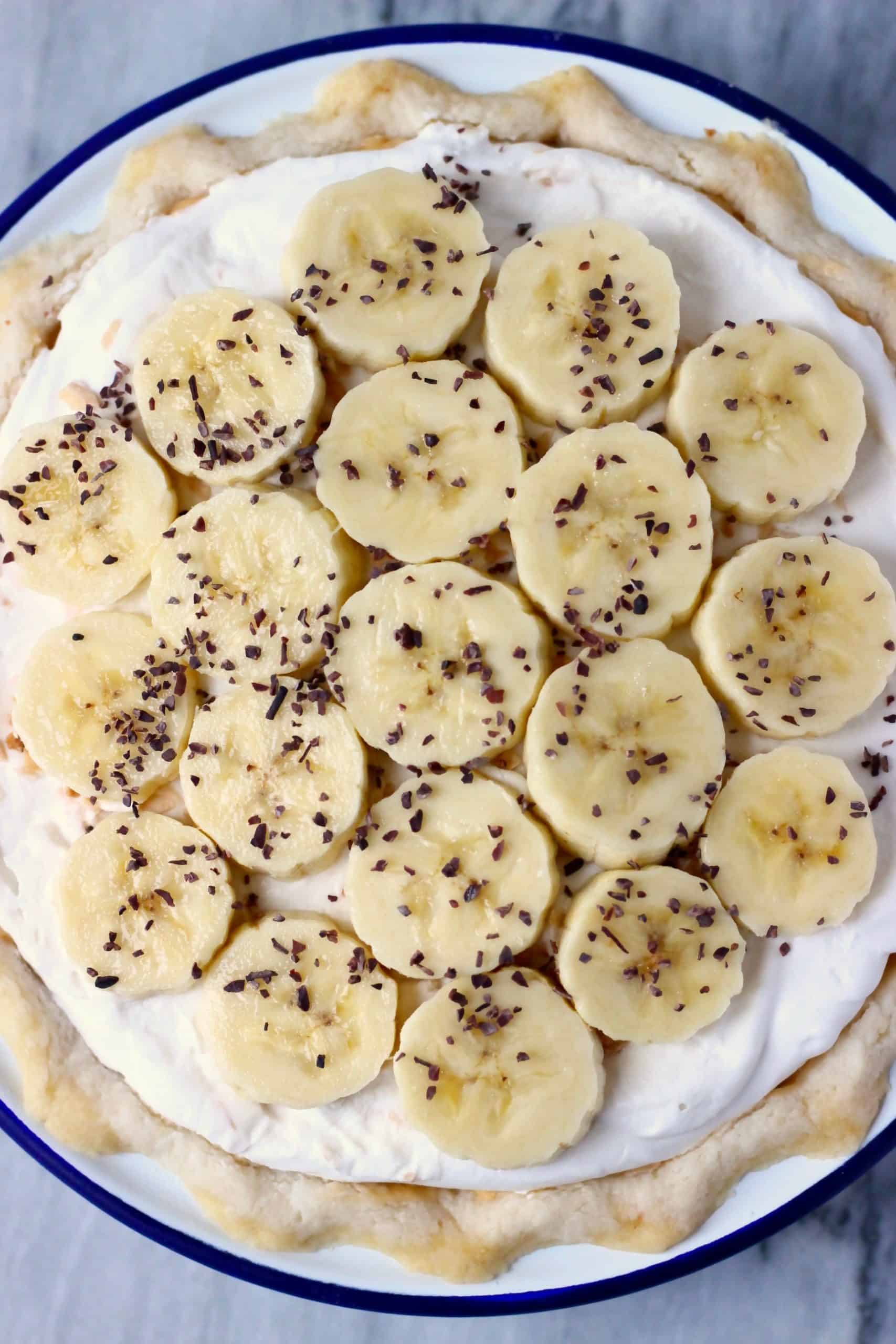 Pastel de crema de plátano vegano sin gluten con crema batida y plátanos en rodajas en un molde para pastel blanco