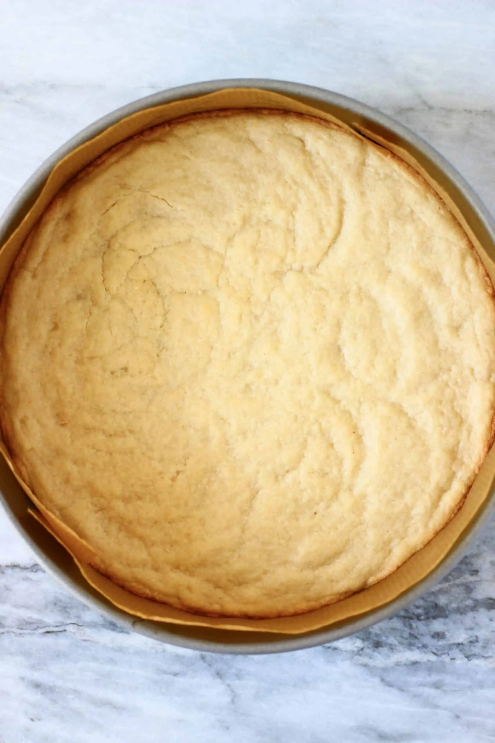 Vegan baked cheesecake crust in a round springform baking tin lined with baking paper