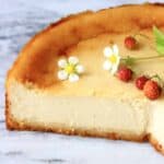 A sliced vegan baked cheesecake topped with wild strawberries and strawberry flowers