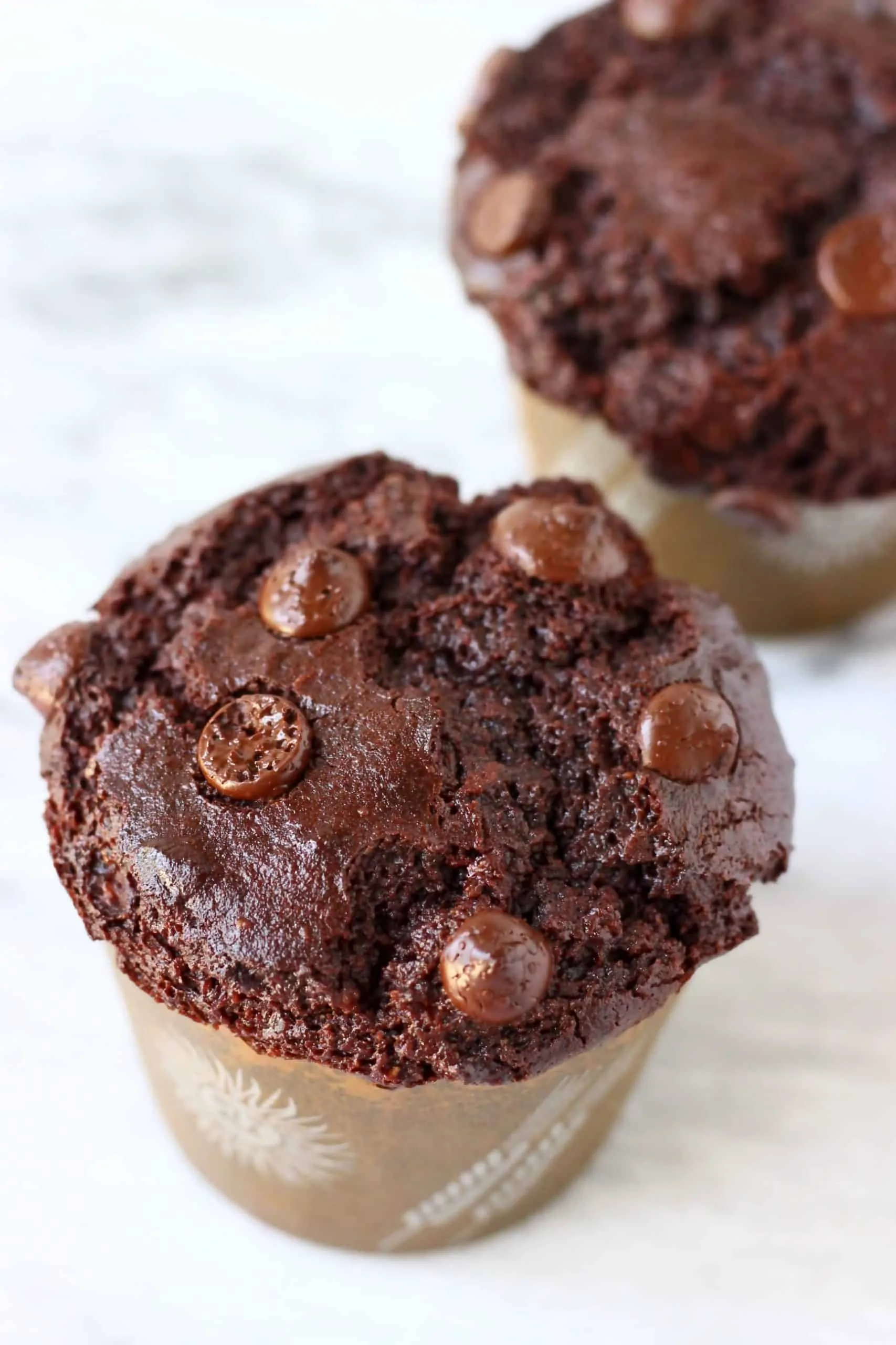 Two gluten-free vegan chocolate zucchini muffins in brown muffin cases