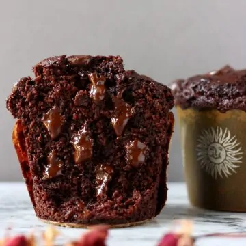 Two gluten-free vegan chocolate zucchini muffins, one cut in half with melted chocolate chips inside
