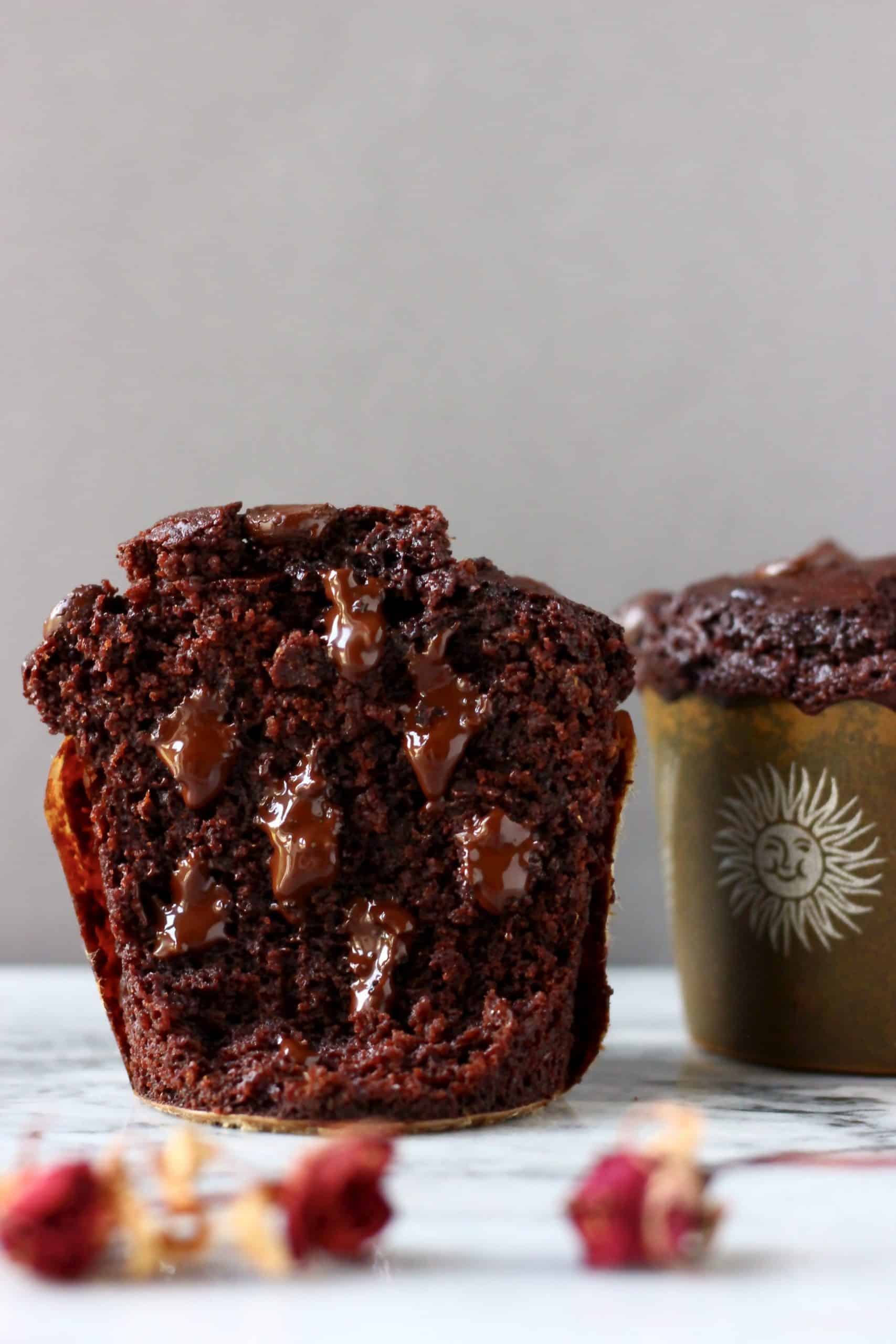 Two gluten-free vegan chocolate zucchini muffins, one cut in half with melted chocolate chips inside