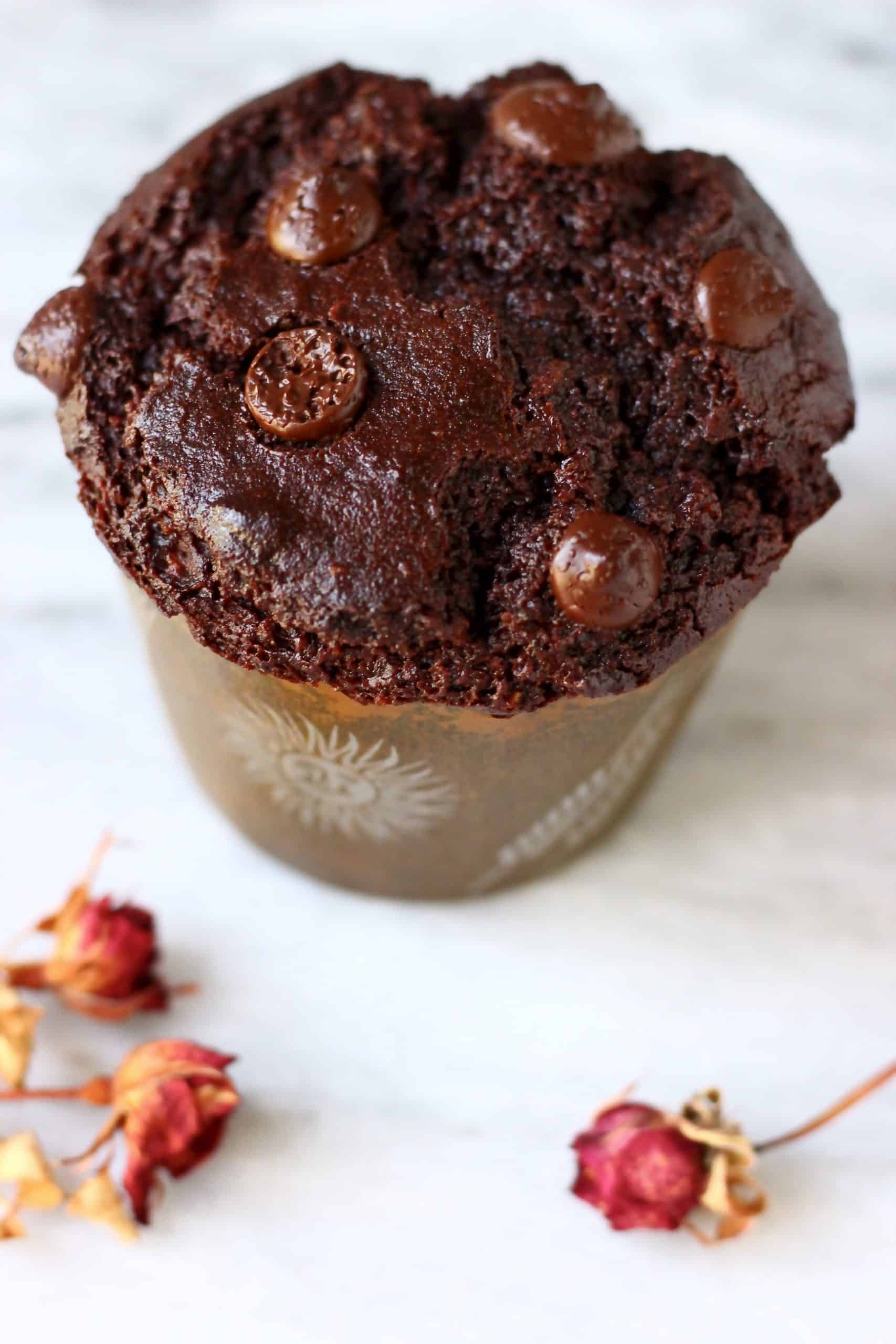 A gluten-free vegan chocolate zucchini muffin topped with chocolate chips in a brown muffin case