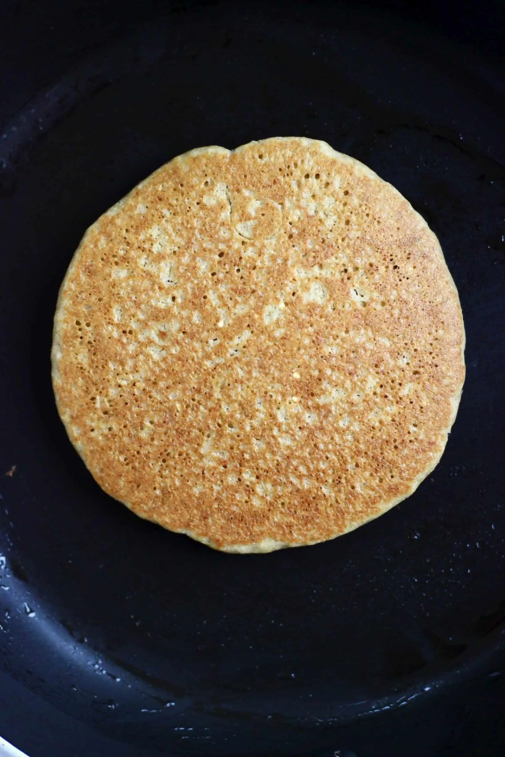 A golden brown quinoa pancake in a black frying pan