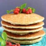 A stack of five quinoa pancakes topped with wild strawberries on a plate