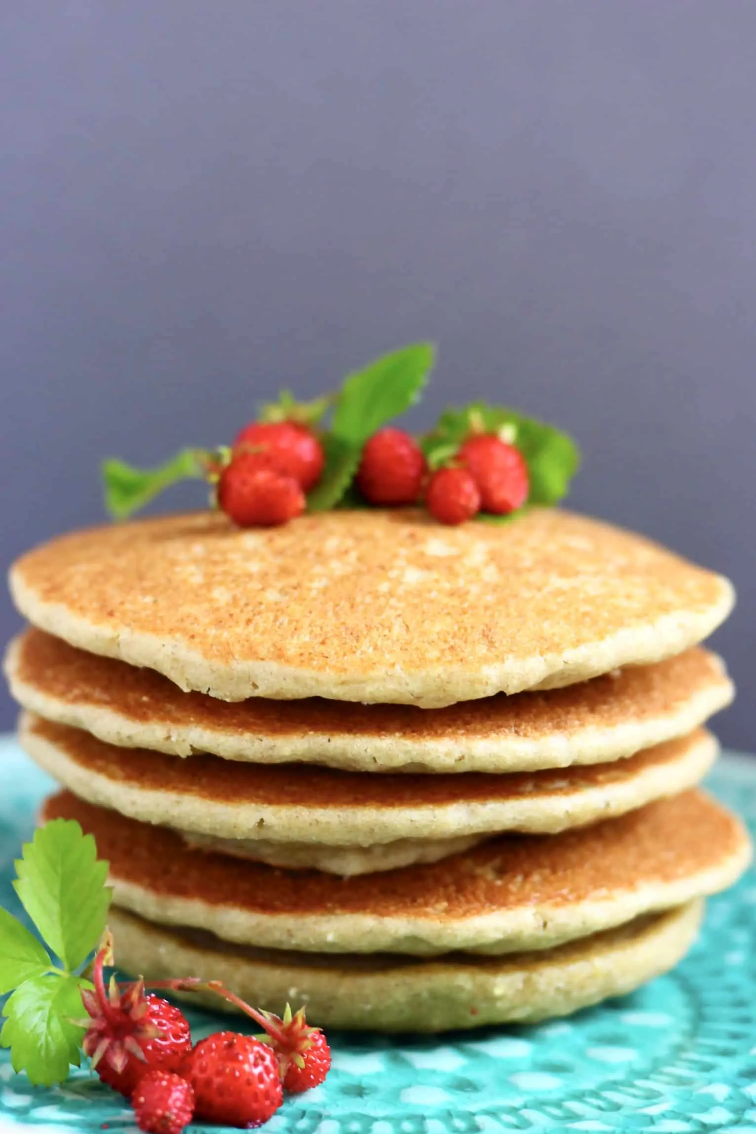 A stack of five quinoa pancakes topped with wild strawberries on a plate