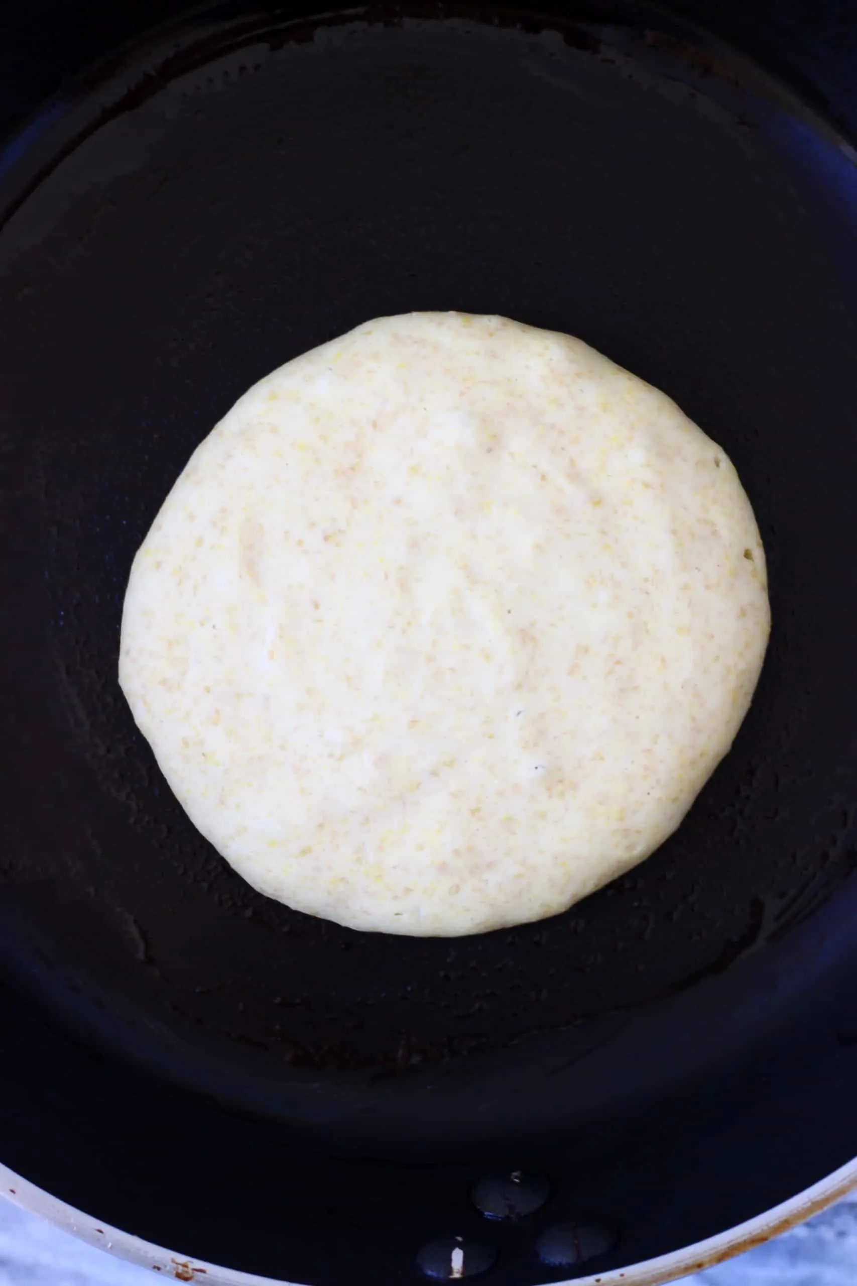 A flaxseed pancake being cooked in a black frying pan