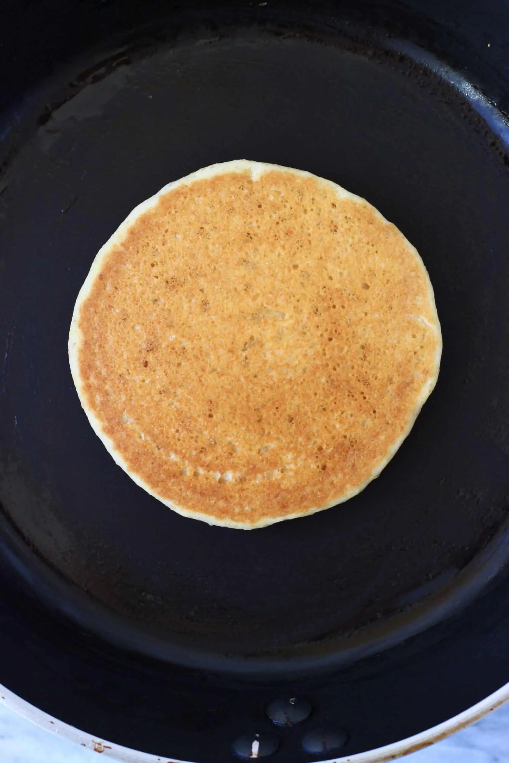 A golden brown flaxseed pancake in a black frying pan