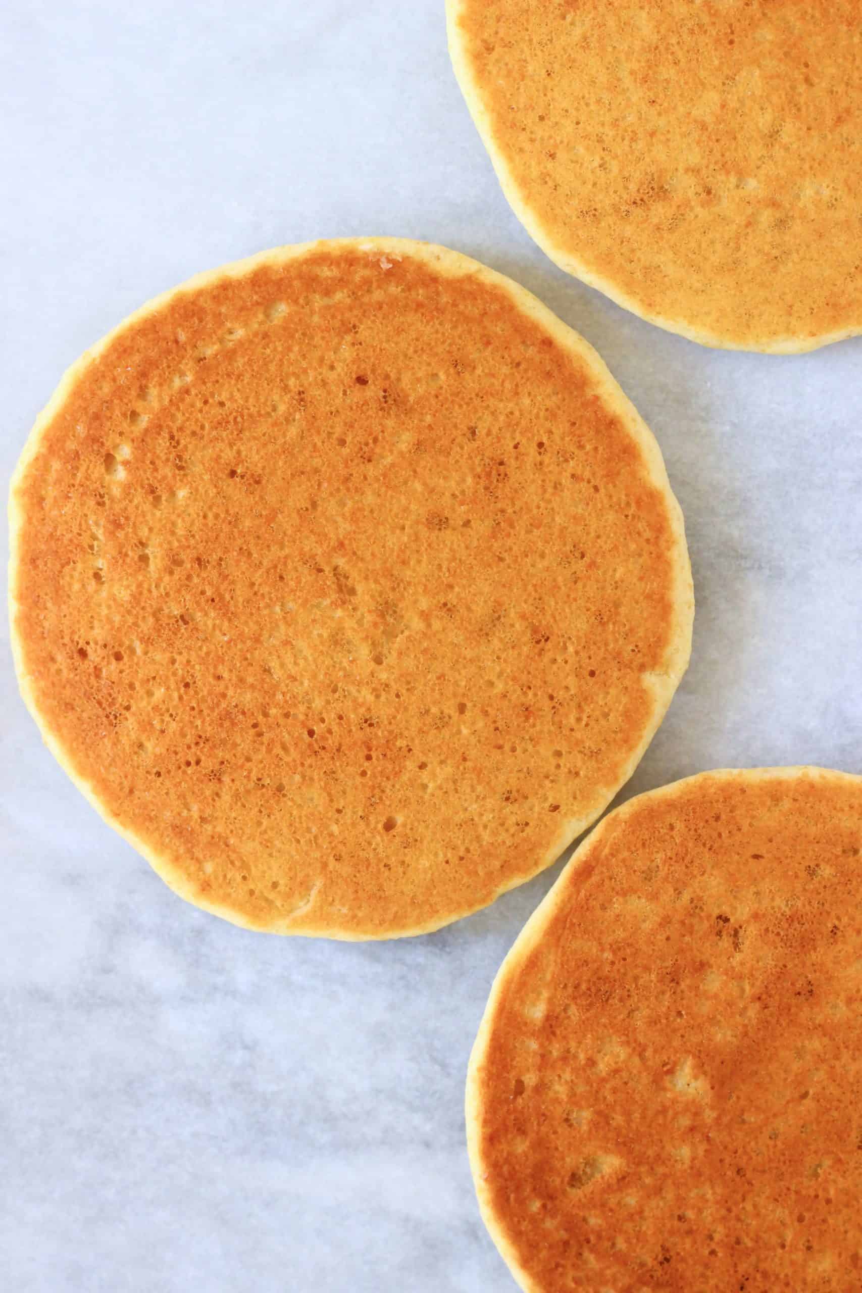 Three golden brown flaxseed pancakes on a sheet of white baking paper