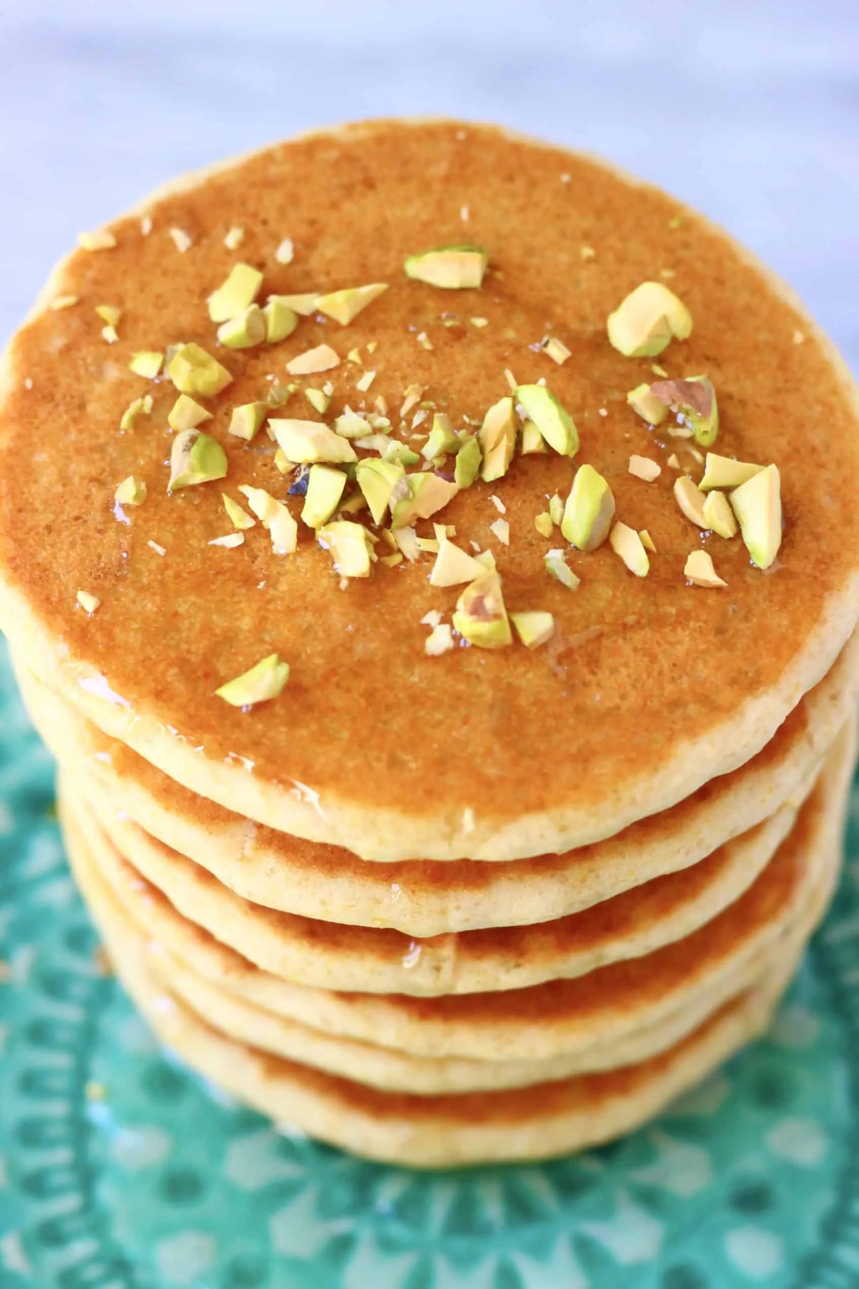 A stack of flaxseed pancakes on a plate topped with syrup and chopped pistachios