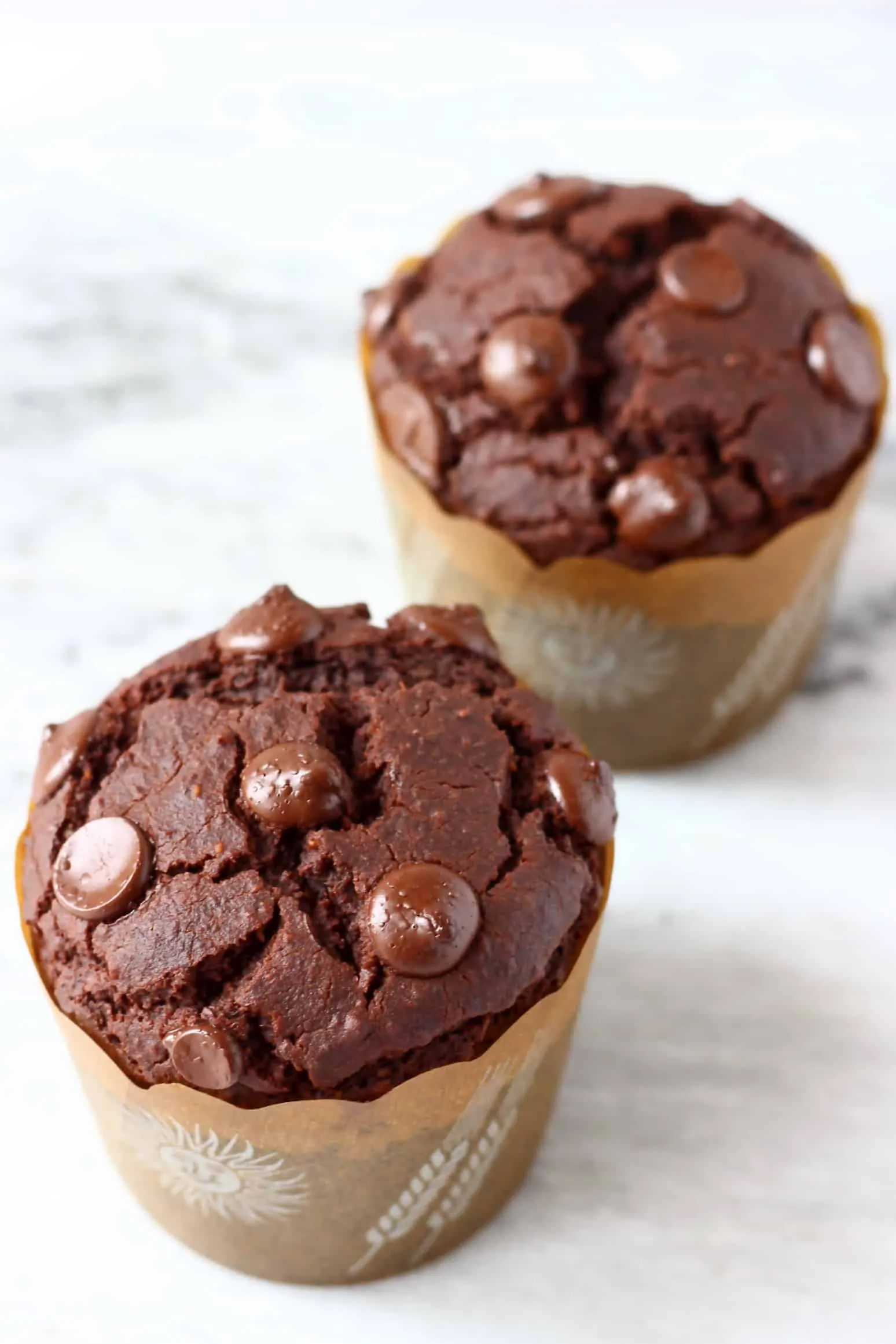 Two gluten-free vegan chocolate pumpkin muffins in brown muffin cases