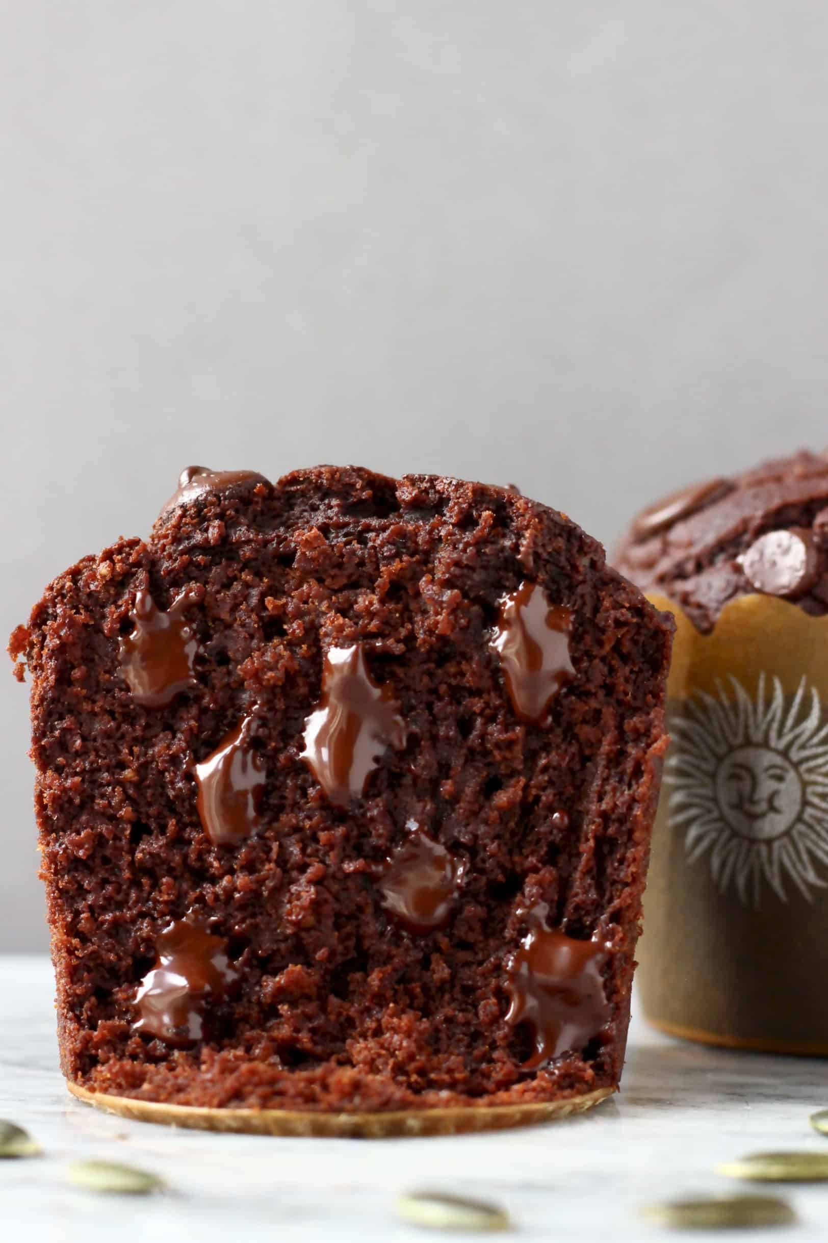 A halved gluten-free vegan chocolate pumpkin muffin on a marble slab with pumpkin seeds