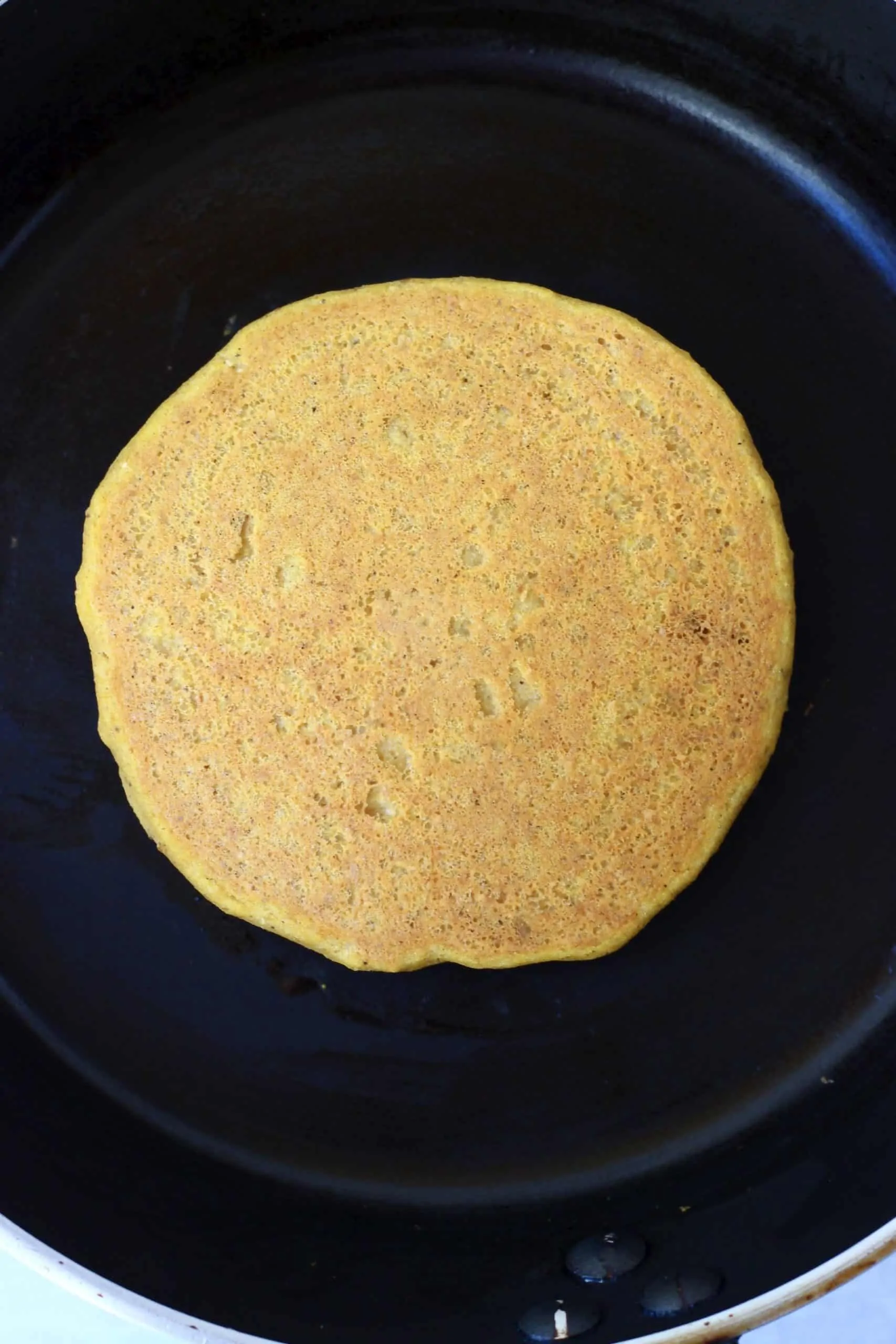 A gluten-free vegan pumpkin pancake in a black frying pan