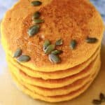 A stack of gluten-free vegan pancakes on a plate topped with syrup and pumpkin seeds