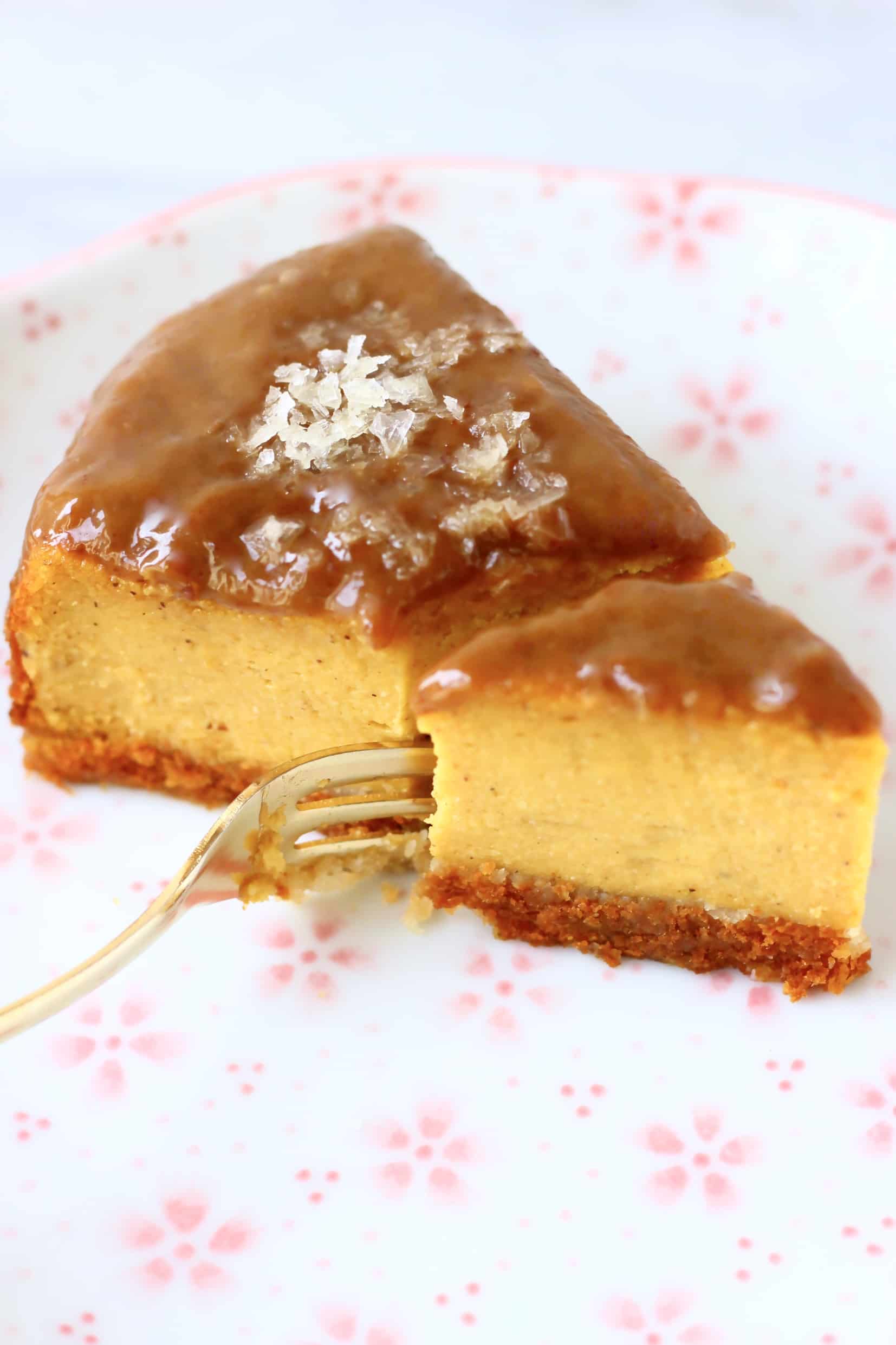 A slice of vegan baked pumpkin cheesecake topped with caramel sauce and salt with a fork taking a bite out of it