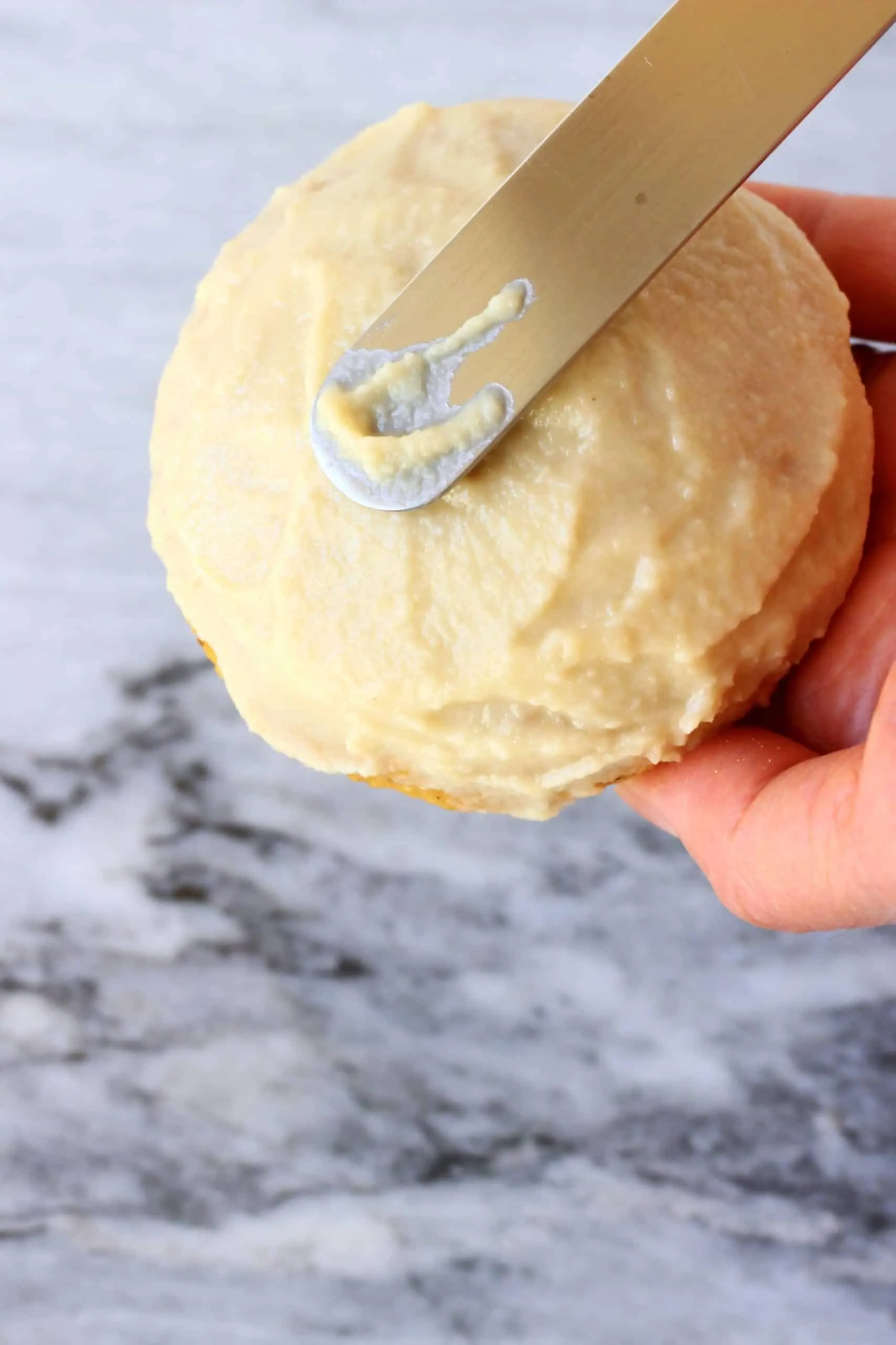 A knife spreading white frosting over a gluten-free vegan pumpkin cookie