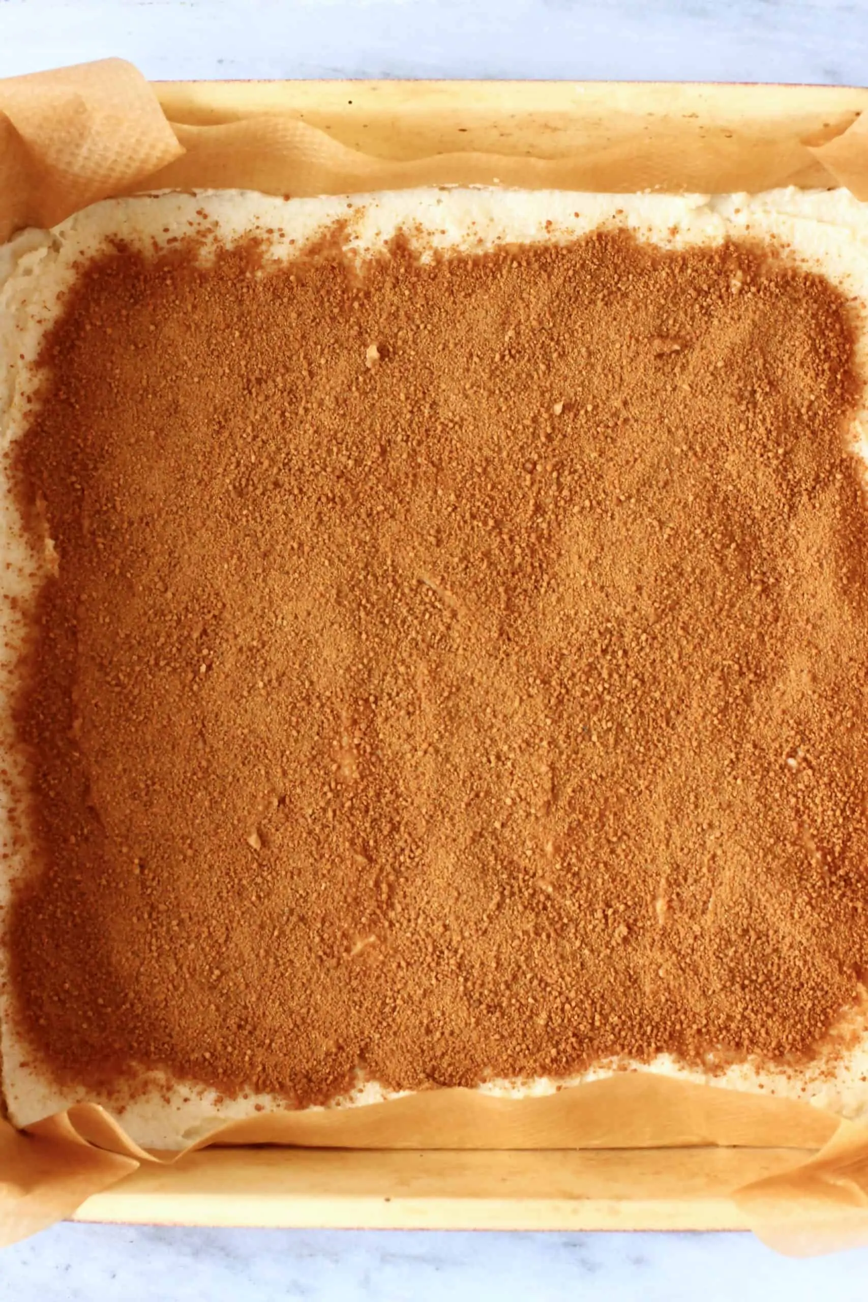Raw vegan coffee cake batter topped with cinnamon and coconut sugar in a square baking tin lined with baking paper