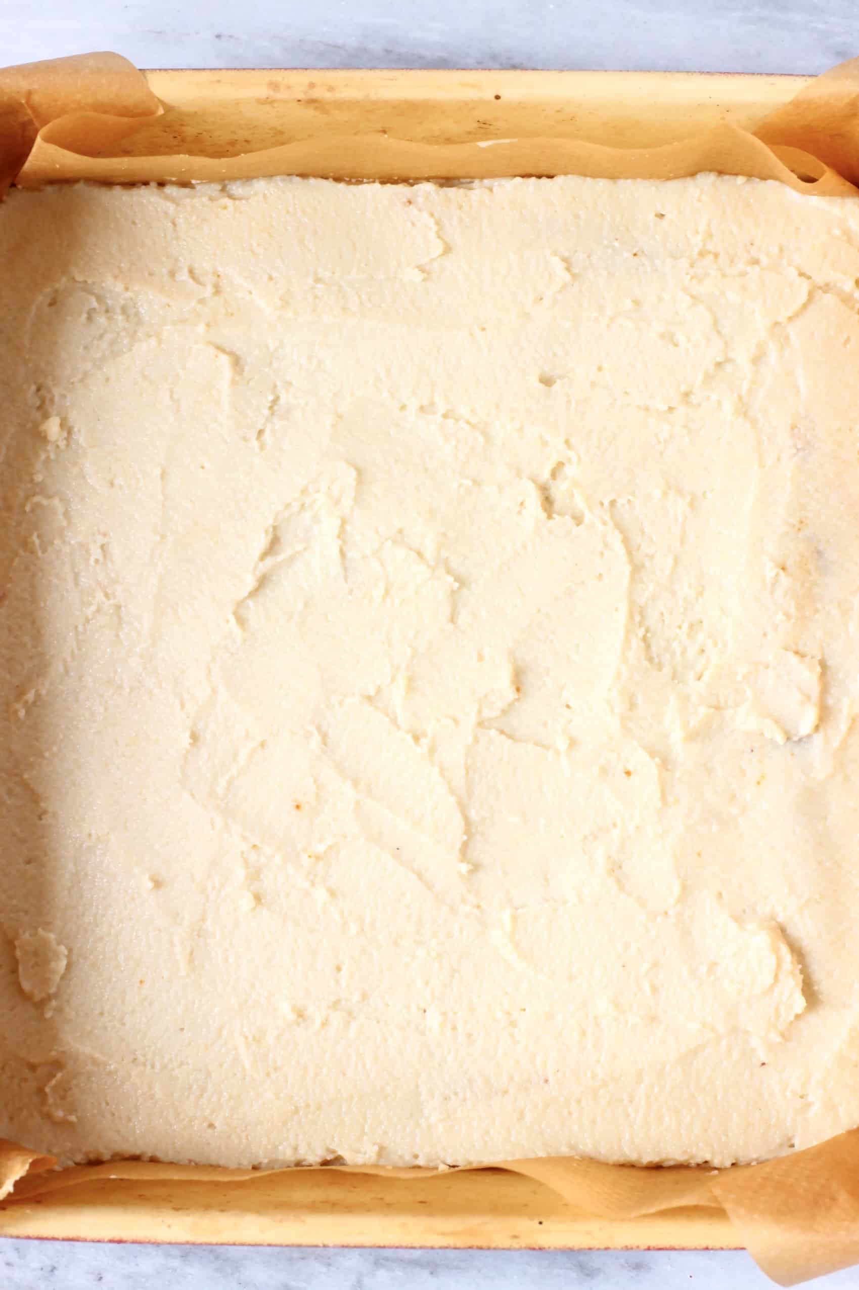 A second layer of raw vegan coffee cake batter in a square baking tin lined with baking paper
