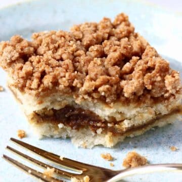 A square slice of vegan coffee cake with cinnamon sugar filling and brown crumble on a plate with a bite taken out of it