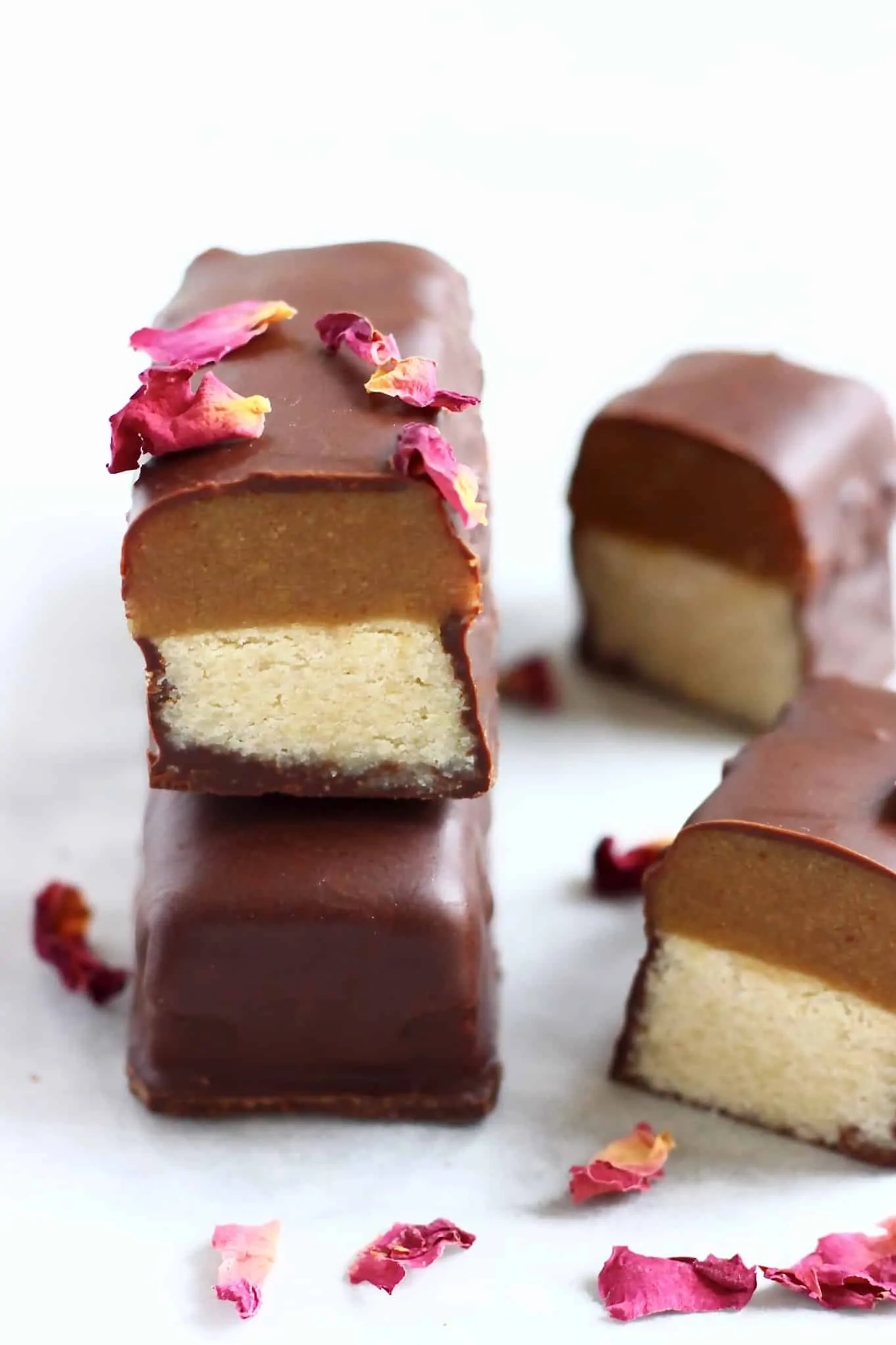 A vegan twix bar cut in half on top of a whole bar decorated with rose petals