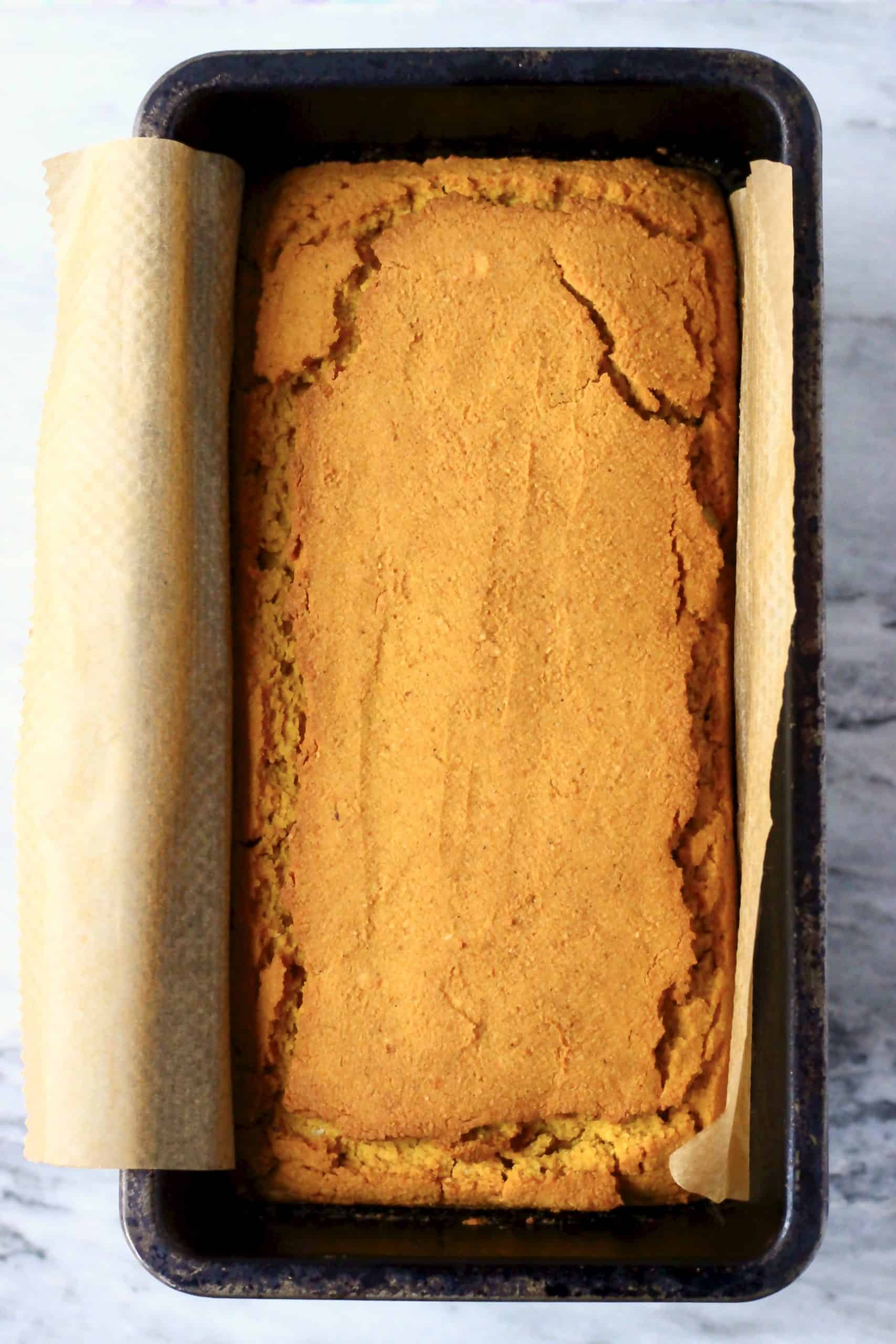 A gluten-free vegan pumpkin loaf cake in a loaf tin lined with baking paper