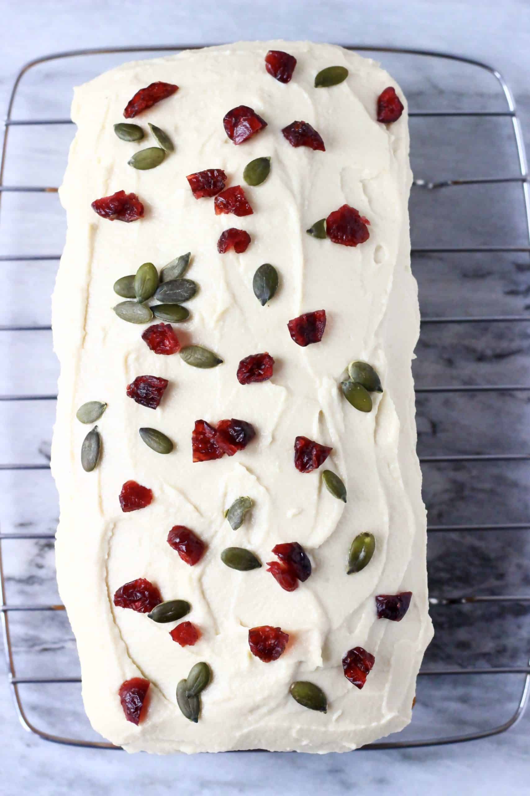 A loaf of gluten-free vegan pumpkin loaf cake topped with cream cheese frosting, dried cranberries and pumpkin seeds on a wire rack