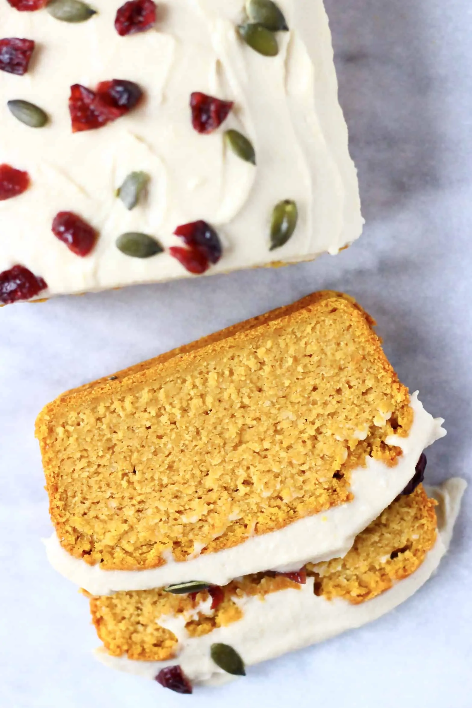 A loaf of gluten-free vegan pumpkin loaf cake topped with cream cheese frosting with two slices next to it