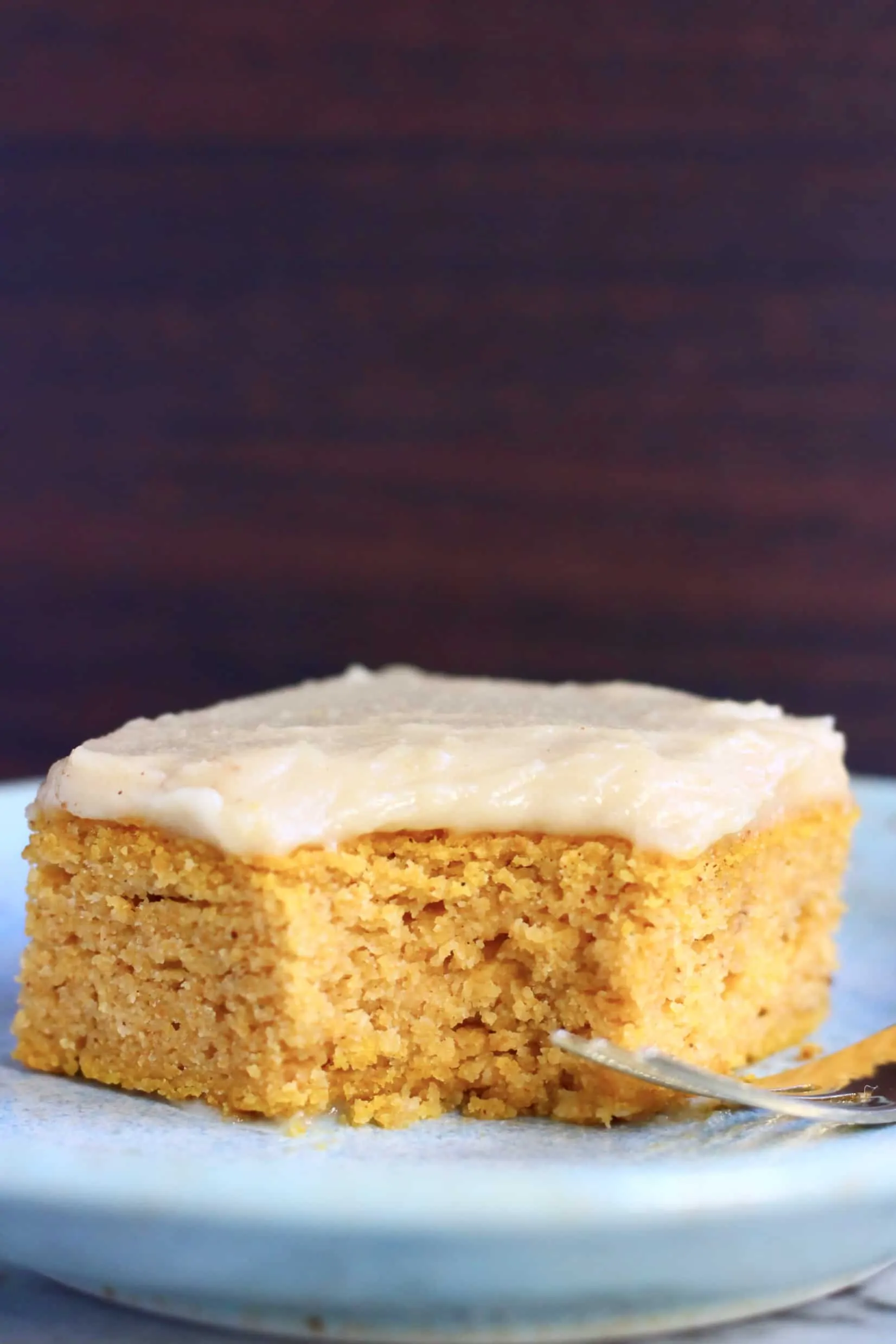 A square of gluten-free vegan pumpkin bars topped with frosting with a mouthful taken out of it on a  plate with a fork