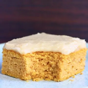 A square of gluten-free vegan pumpkin bars topped with frosting with a mouthful taken out of it on a blue plate