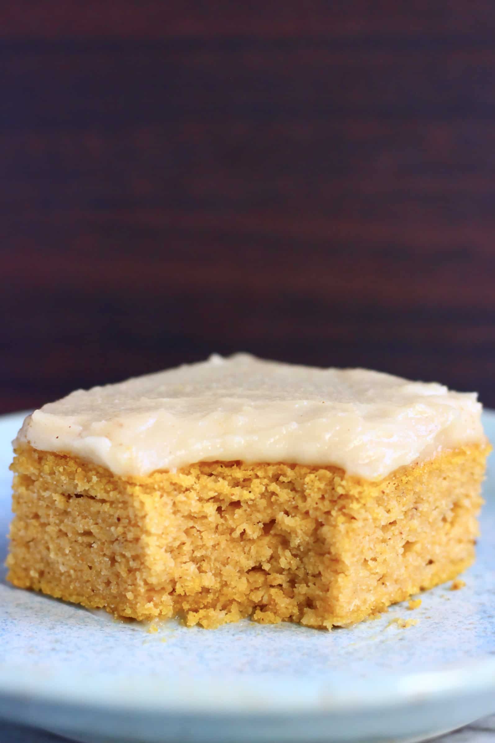 A square of gluten-free vegan pumpkin bars topped with frosting with a mouthful taken out of it on a blue plate