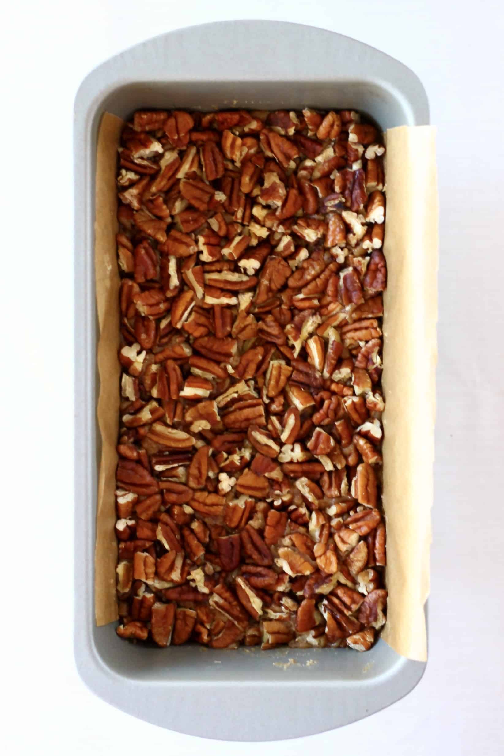 Vegan pecan pie bars base and filling topped with pecans in a loaf tin lined with baking paper