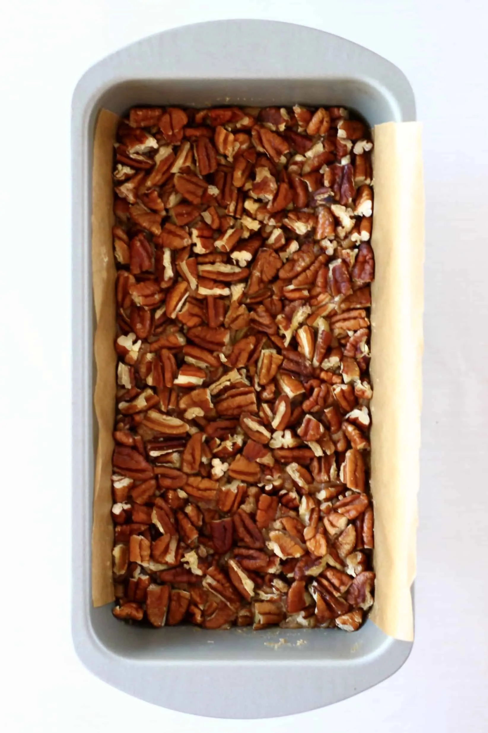 Vegan pecan pie bars base and filling topped with pecans in a loaf tin lined with baking paper