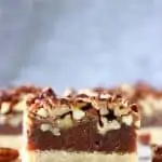 Three vegan pecan pie bars with a pie crust base, date caramel filling and topped with pecans